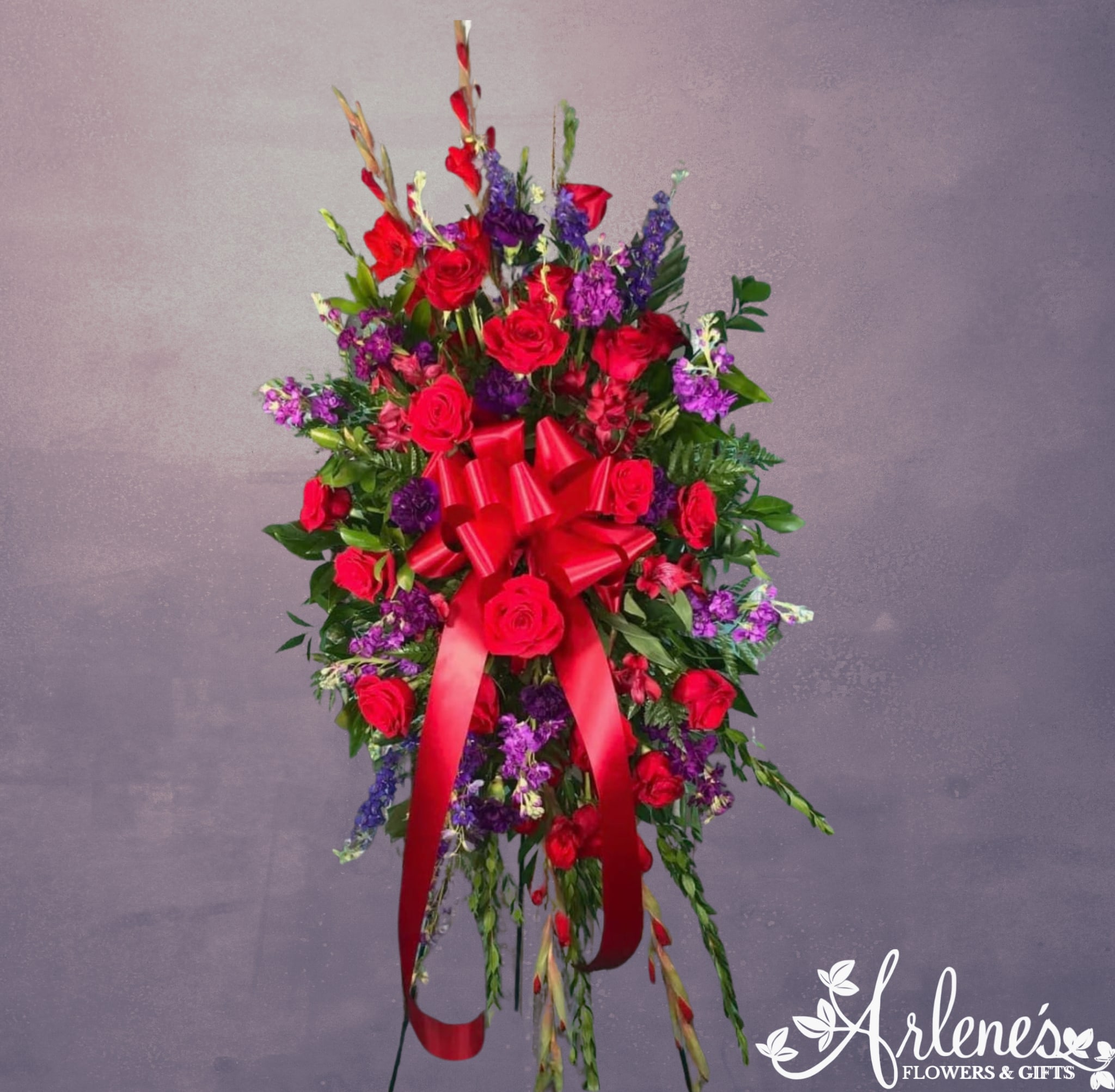 Standing spray of red roses and purple flowers with a large red bow on an easel