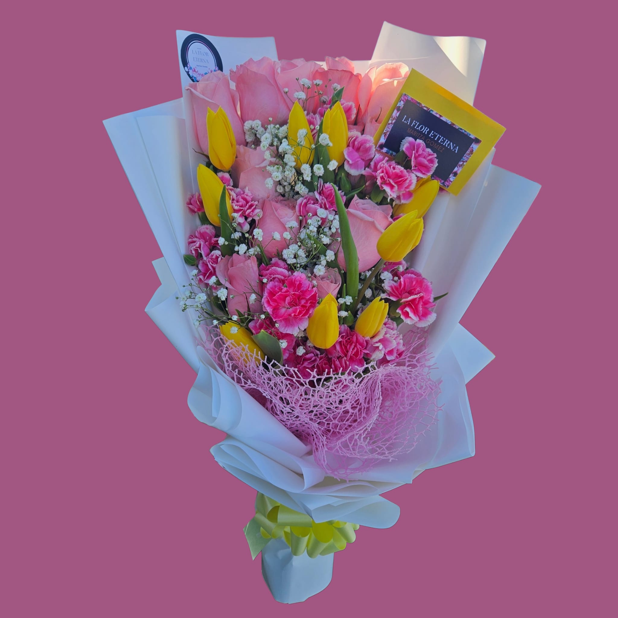 Pretty pink  - A lush cluster of soft pink roses takes center stage in this hand-tied bouquet, surrounded by bright yellow tulips and vivid hot-pink carnations for a cheerful, affectionate look perfect for a birthday bouquet, anniversary roses, or a celebratory romantic gesture. The mix of pinks and sunny yellow reads joyful and intimate-she'll feel noticed and celebrated the moment the wrapping unfolds.  Dense, tactile blooms are accented with small white filler flowers and arranged with clean, contemporary lines thanks to structured white paper with crisp folded edges. A layer of pink mesh netting near the base adds playful texture, finished with a yellow ribbon, attached greeting card, and round label sticker for a polished presentation. Ideal for sending warm congratulations, saying "I'm thinking of you," or marking a special date; hand-tied for easy display and ready to place in a vase upon arrival.