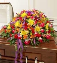 Life Time Memories Multicolor - A bright, full casket spray that brings warmth and celebration to a memorial or funeral service, Life Time Memories Multicolor uses bold color to honor a life well lived. This low, elongated mound-style arrangement places the product type and the occasion-sympathy and funeral-front and center, offering a comforting, uplifting visual that helps the person you're remembering feel cherished and vividly present.  Densely layered yellow spider-style chrysanthemums, orange lilies, and red and pink roses form a saturated field of color and texture, with snapdragons adding vertical interest through the composition. The spray rests directly on a polished wooden casket and is finished with curled purple ribbon flowing from the center, giving graceful movement and a thoughtful contrast to the warm tones. Sized and shaped for formal presentation, it creates an immediate visual focus at a memorial service while remaining appropriate for a celebration-of-life setting.  Designed to convey heartfelt remembrance and joyful reflection, this casket spray is a meaningful way to honor someone who loved bright, lively color. Ask for delivery timing and placement details when ordering so the arrangement arrives ready for the service; standard care is to keep flowers cool and sheltered before presentation to maintain their fresh, vivid appearance.
