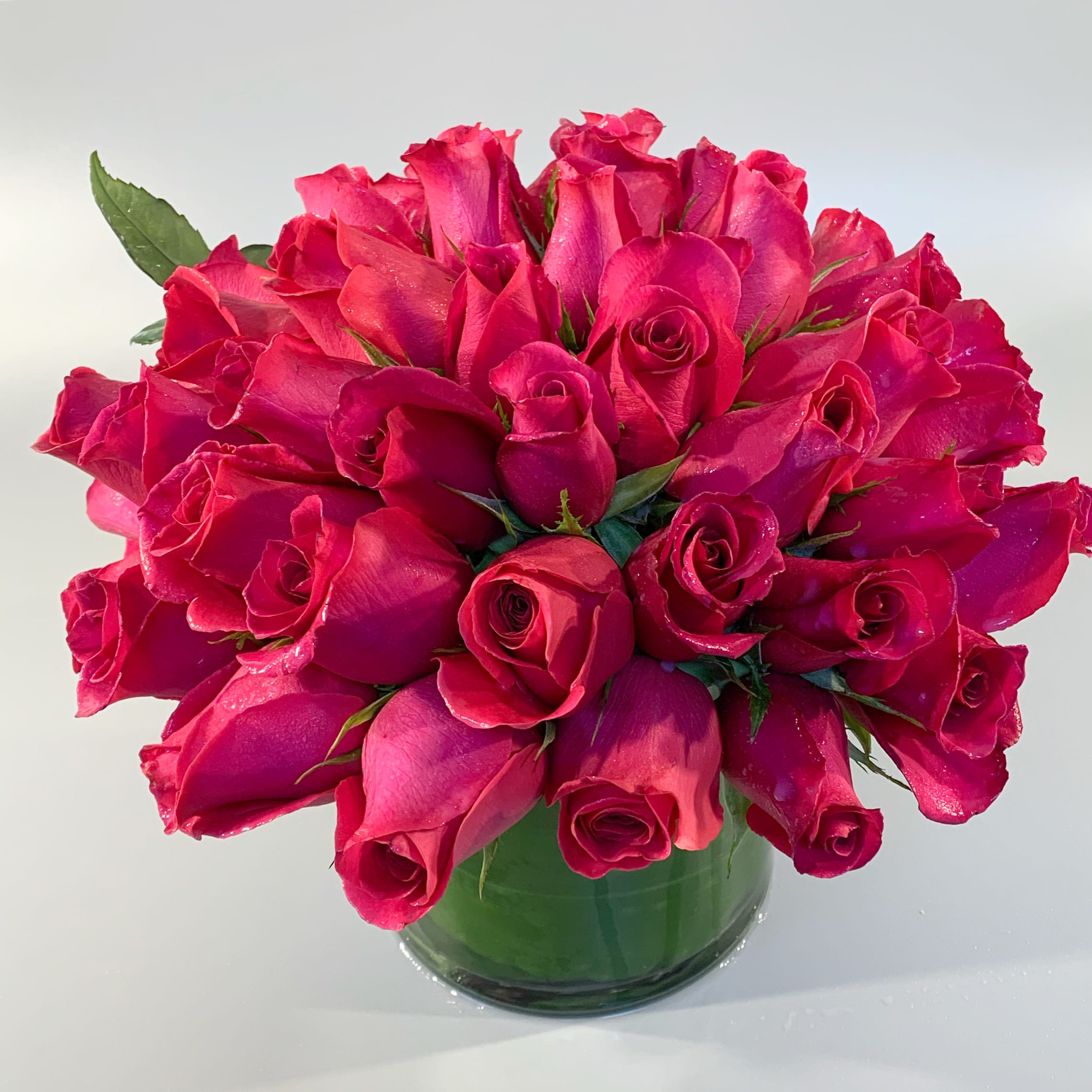AMOUR - A modern, lush, luxurious hand-tied arrangement of nearly 50 fresh roses designed in a clear leaf-lined glass vessel. Also available with white, pink or yellow roses. Please specify any changes in the special instructions. 