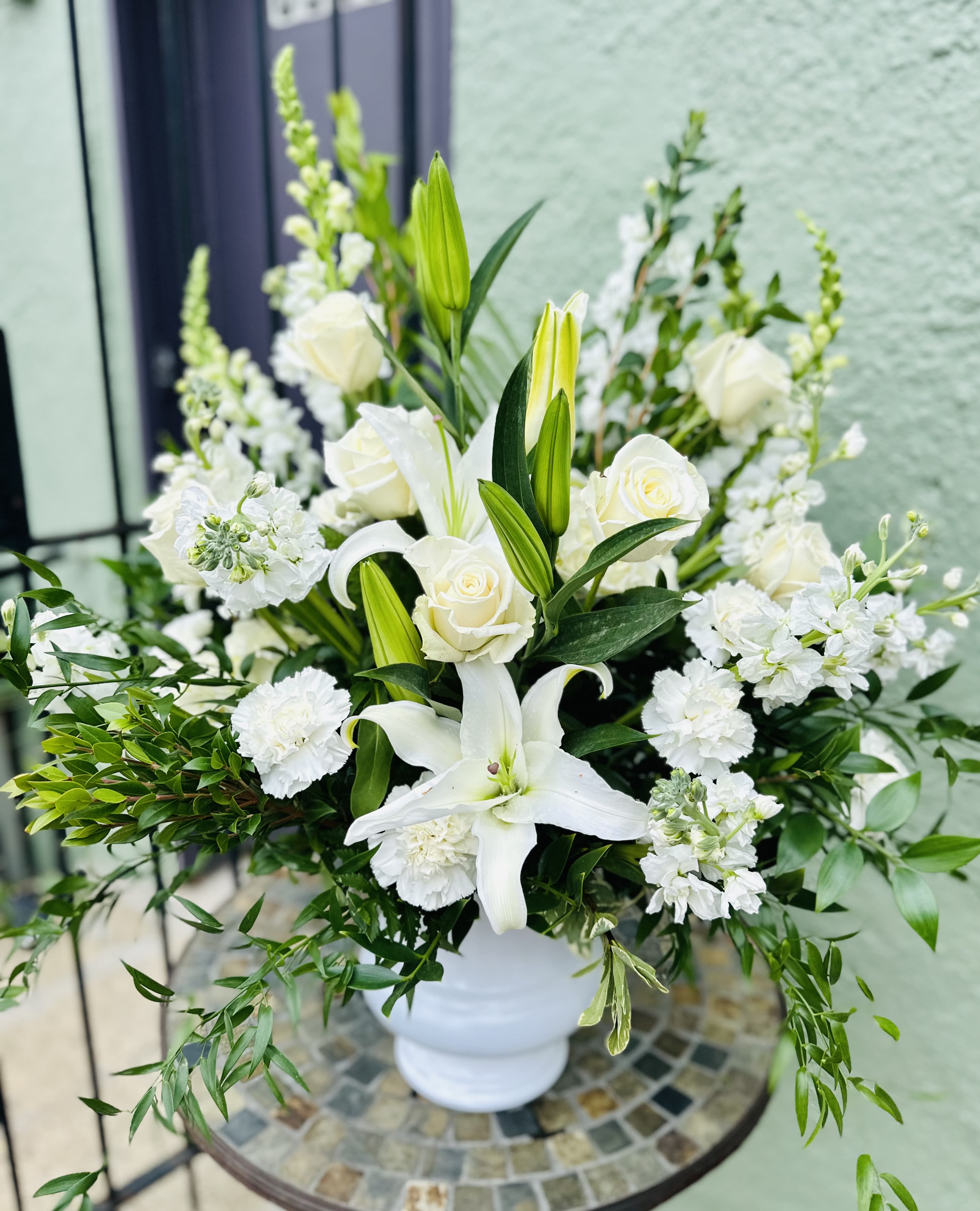 Sincere Serenity - A simple and elegant display of pure white blossoms such as roses, Asiatic lilies and carnations, presented in a classic urn, creates a serene and contemplative display. A traditional choice for any service or wake.  Approximately 24" (W) x 26" (H) Orientation: One-Sided