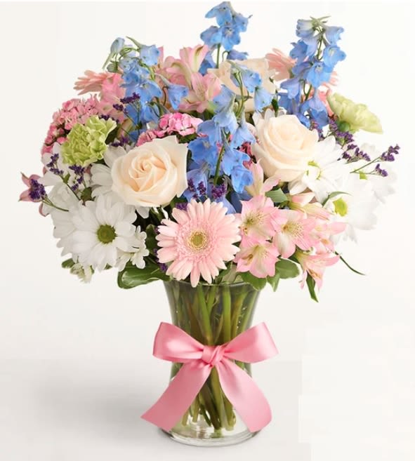 Watercolor Skies Bouquet - the blue delphinium, is dazzling on its own. Surrounded by roses, Peruvian lilies, and other blooms, in a vase wrapped with a pink satin ribbon, it’s even more alluring.