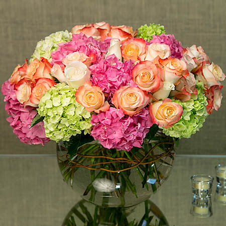 Low round arrangement of peach roses and pink and green hydrangeas in a clear glass bowl vase