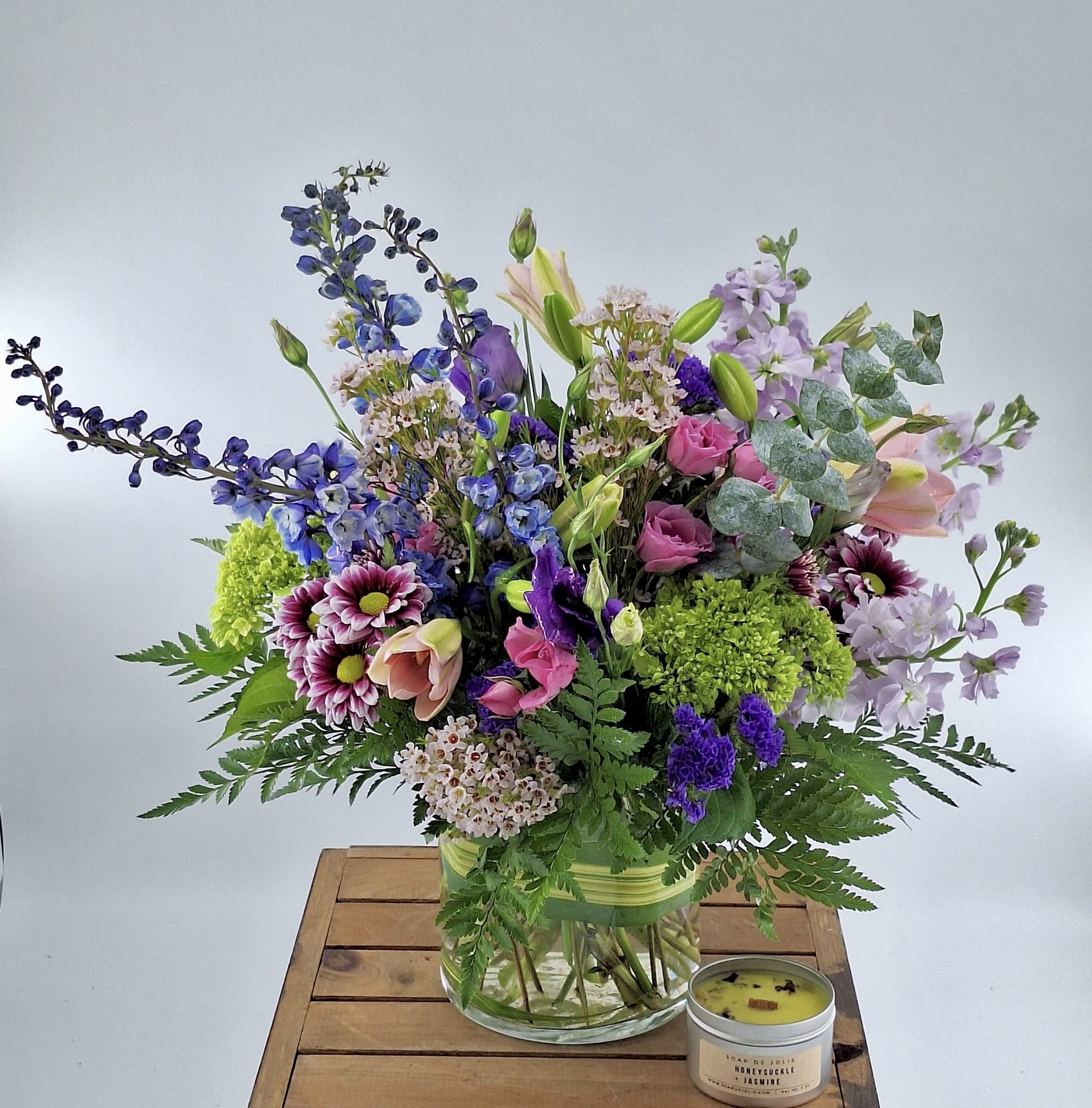 Purple Dream (BR) - Immerse yourself in elegance with our modern bouquet featuring blue delphinium, spray roses, purple lisianthus, pink lilies, mini green hydrangeas, waxflower, and eucalyptus. Expertly arranged in a glass cylinder vase, it’s crafted to brighten your special moments beautifully. 