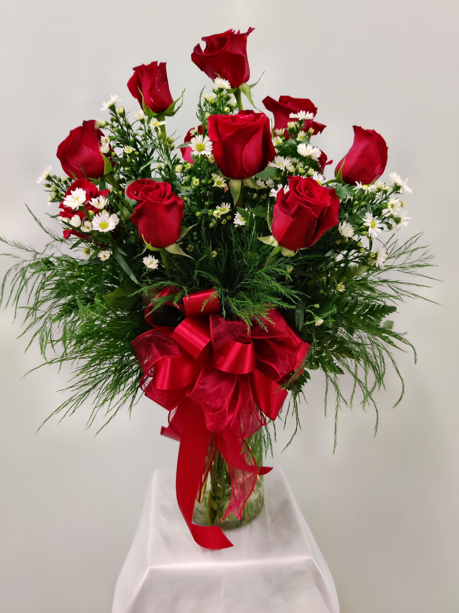 A Dozen Reasons Why - Long-stemmed red roses paired with white filler flower create a classic, expressive bouquet that says love, celebration, or comfort-perfect as a birthday bouquet, anniversary roses, or a Mother's Day gift. The clear glass vase shows the gathered stems and adds an elegant, timeless feel; a large red satin ribbon bow gives the arrangement a romantic finish that also suits Valentine's Day, Father's Day, or "just because" moments.  Vase dimensions and exact stem lengths vary by local florist; simple care-fresh water and a cool spot out of direct sun-will keep blooms looking their best.