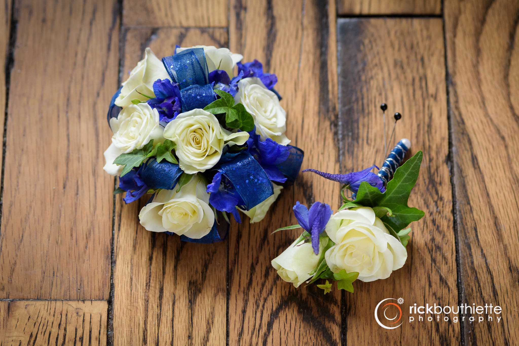 White &amp; Blue Combo - Shown as Standard. White spray roses, navy delphinium and ivy come designed on a pearl bracelet with accenting blue ribbon. Boutonniere to match. *We custom design this arrangement and use the freshest flowers available the day of delivery. The arrangement in this picture is an example of the size and style and may not feature the exact product shown.*