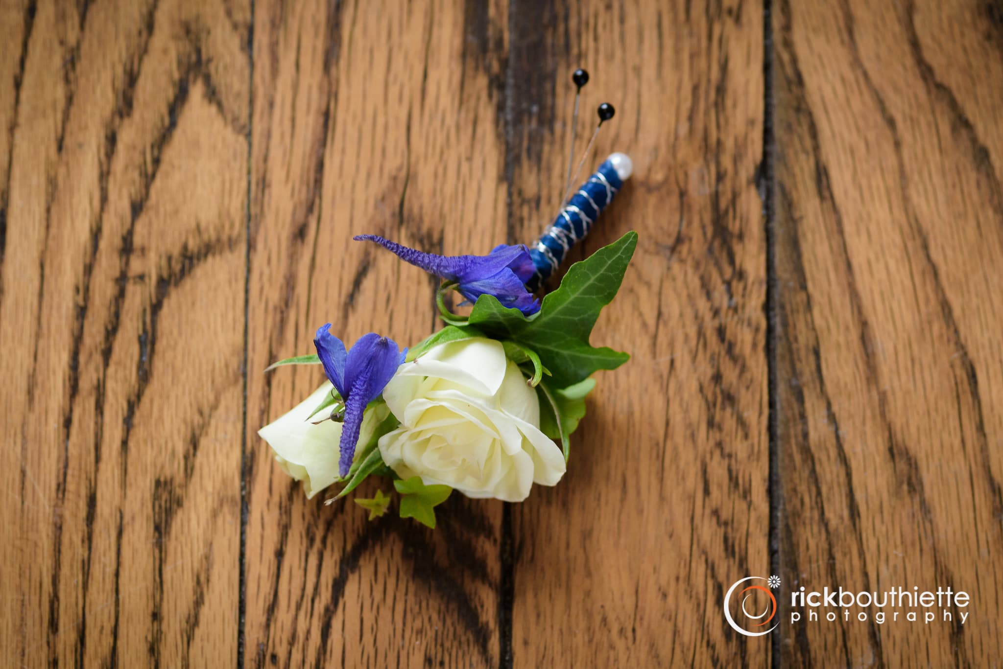White &amp; Blue Boutonniere - Shown as Standard White spray roses and blue delphinium come wrapped in accenting blue ribbon. *Pick up only* *We custom design this arrangement and use the freshest flowers available the day of delivery. The arrangement in this picture is an example of the size and style and may not feature the exact product shown.*  