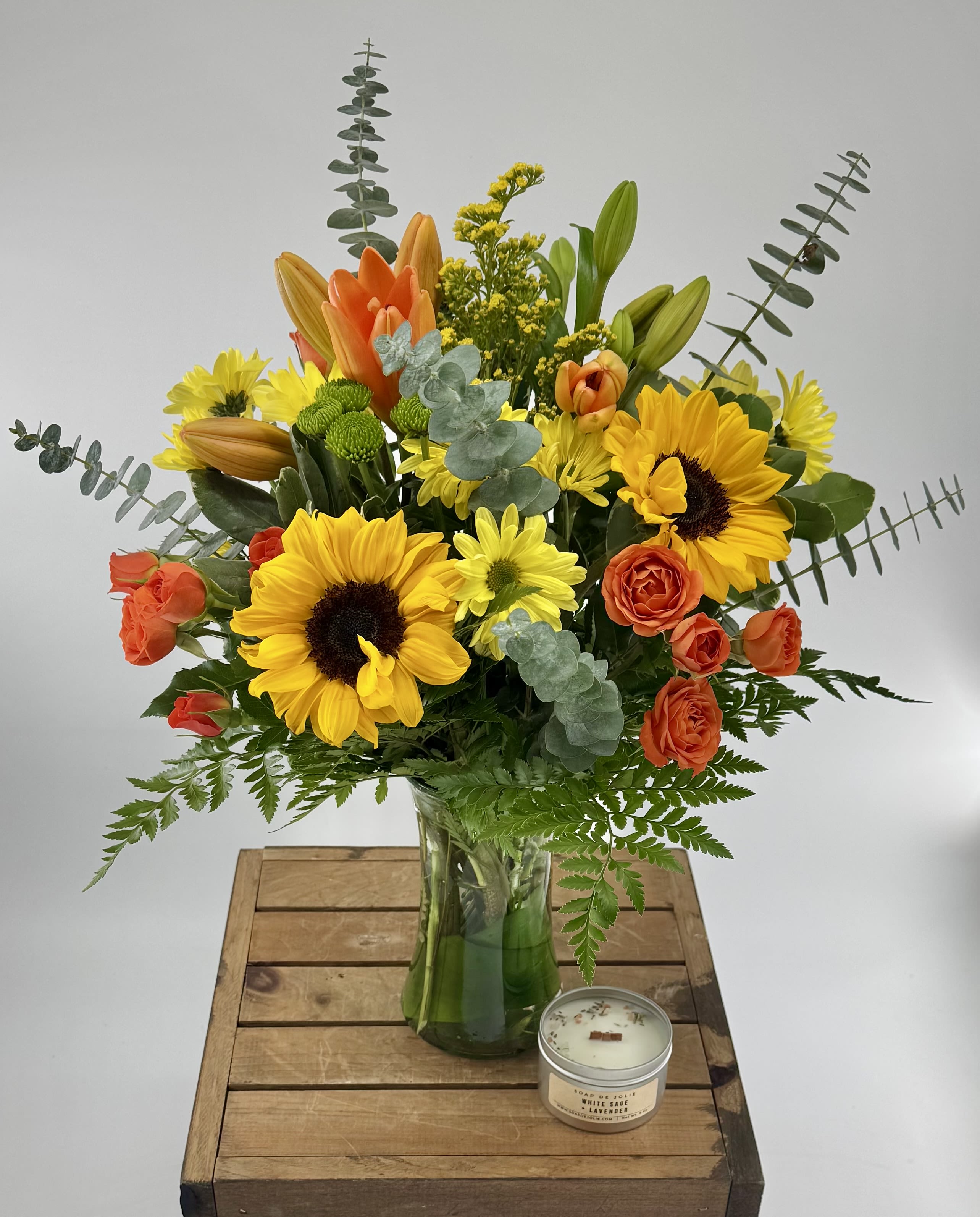 Bouquet of sunflowers, orange roses, and lilies in a glass vase
