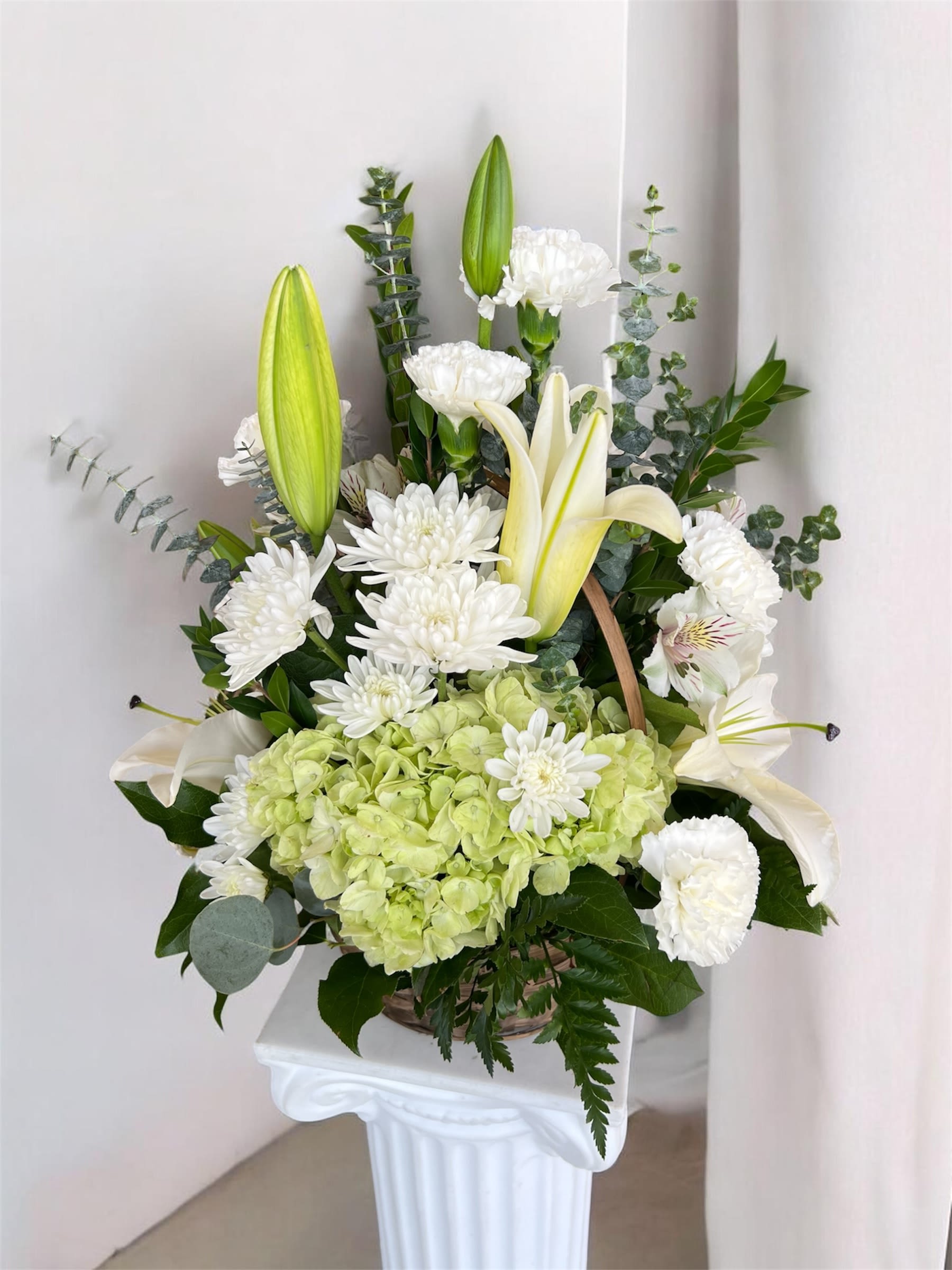 Classic White Basket (medium) - A graceful basket arrangement featuring elegant white blooms and soft green hydrangeas, accented with lilies and fresh greenery. This design offers a serene and timeless look, perfect for expressing sympathy, comfort, and remembrance. 
