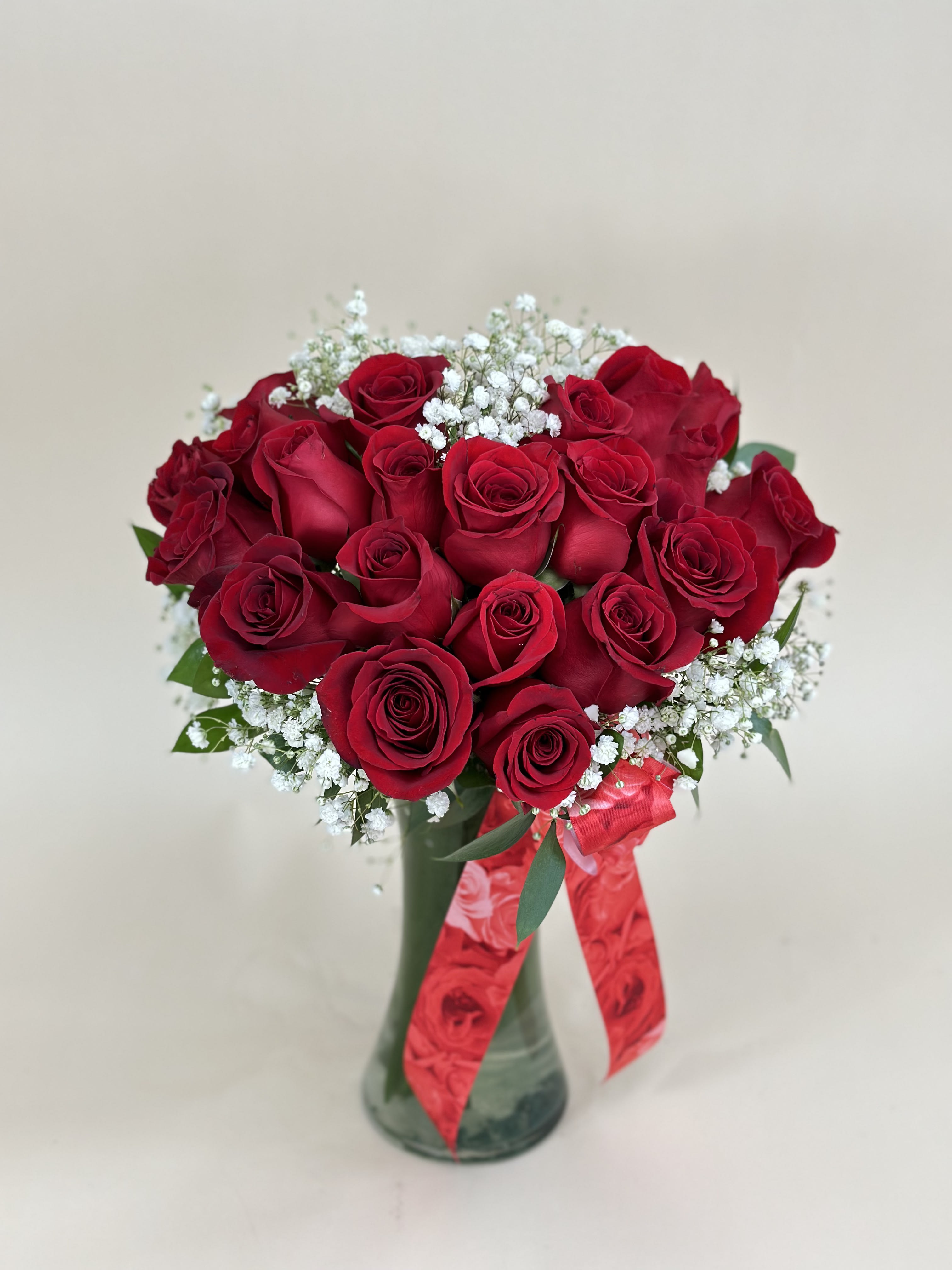 Arrangement of red roses with white filler flowers in a glass vase with a red ribbon