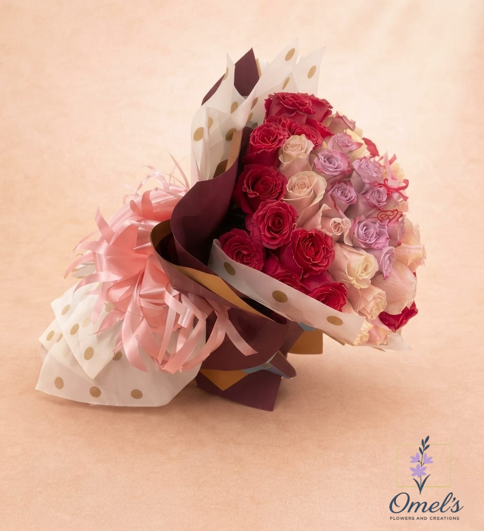 Midnight Blush - A lush dome of mixed roses in hot pink, blush and soft lavender makes a bold romantic statement - perfect as an anniversary bouquet, Valentine's gift, or birthday surprise for the person you want to feel adored. The tightly clustered, hand-tied design reads full and abundant at first glance, so they'll notice the rich color contrast and the velvety texture of each bloom the moment it's presented.  This arrangement pairs full-size roses with spray roses for depth and movement, arranged in a rounded, garden-style dome. Layers of burgundy and gold-toned wrap are finished with white cellophane printed with gold polka dots for a playful, polished presentation, and a large pink satin ribbon bow with curled strands gives the bouquet a festive, gift-ready look. The overall palette - pink, white and lavender - creates a warm, affectionate mood that reads both celebratory and intimate.  Choose this for romantic milestones, heartfelt apologies, or to mark a special birthday; it's the kind of bouquet that makes someone feel truly seen and celebrated. Hand-tied and ready to gift - no additional vase needed - simply trim stems and refresh water if transferring to a vase to extend bloom life.