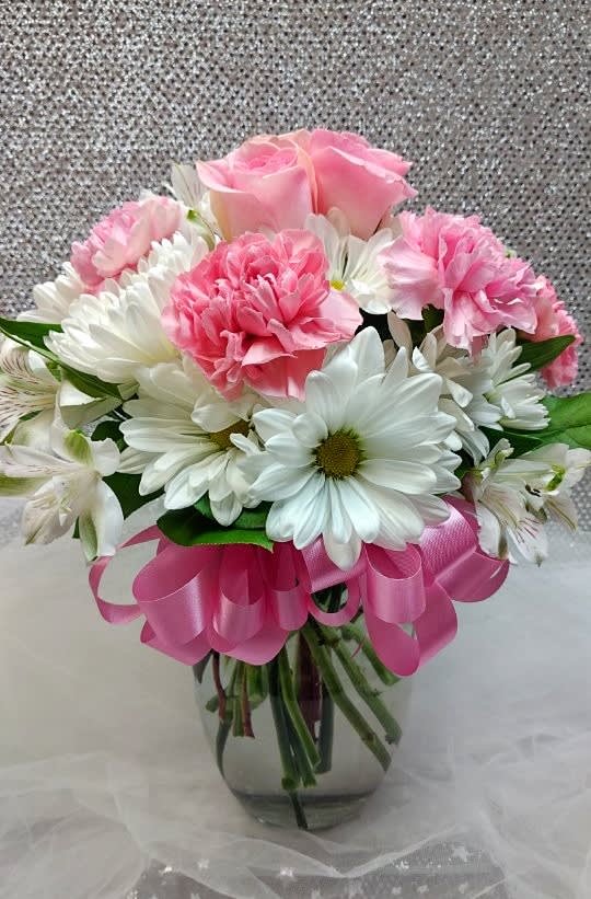 Pink roses and carnations with white daisies in a glass vase with a pink ribbon bow