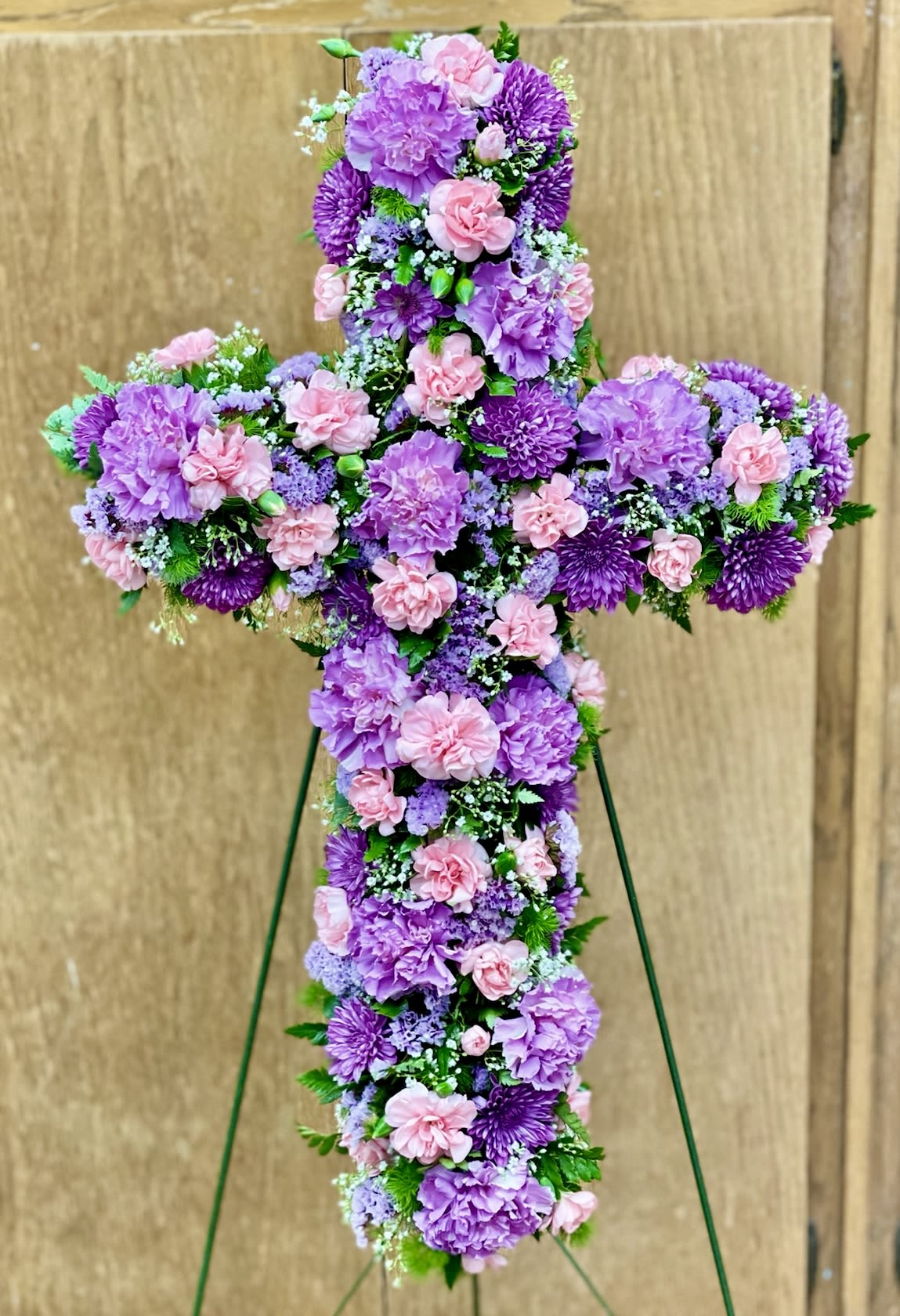 Standing floral cross of lavender and pink blooms on a wire easel