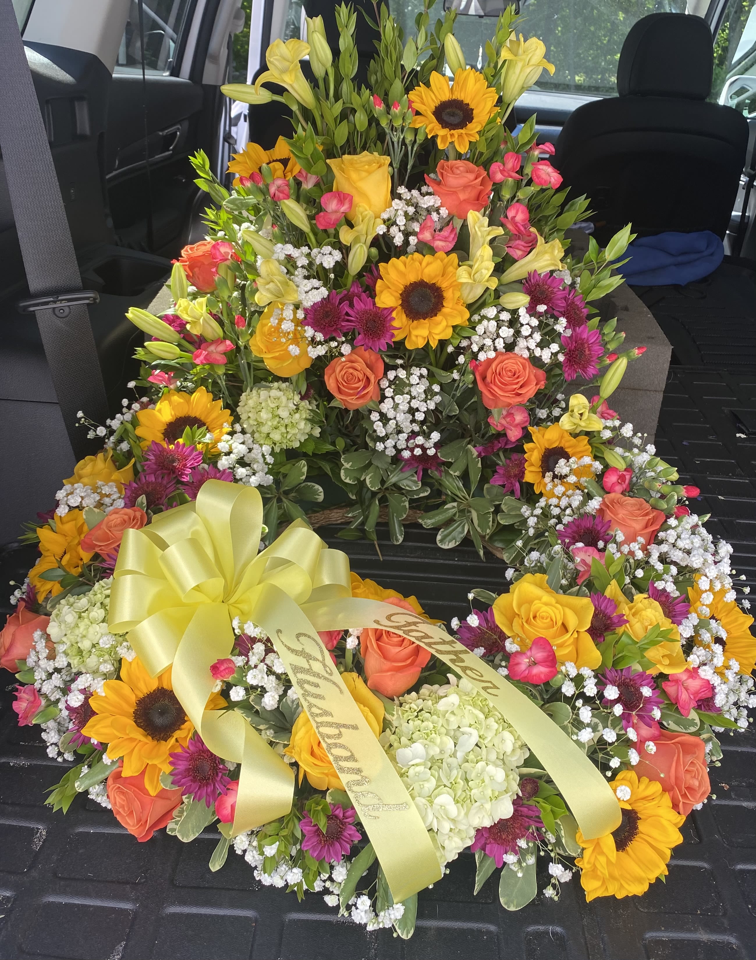 Bright heart-shaped funeral wreath with sunflowers, roses, and a yellow ribbon