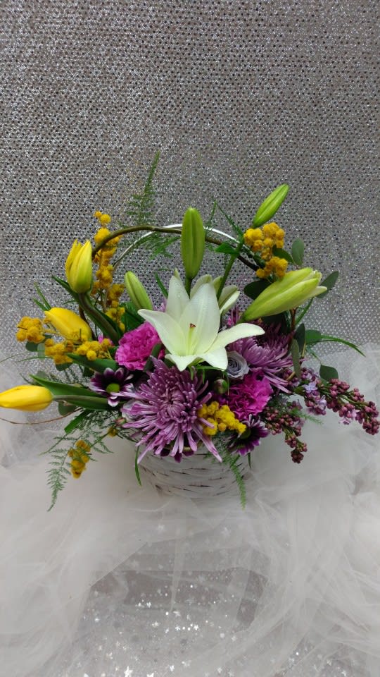Basket arrangement with white lily, purple mums, pink carnations, and yellow tulips.