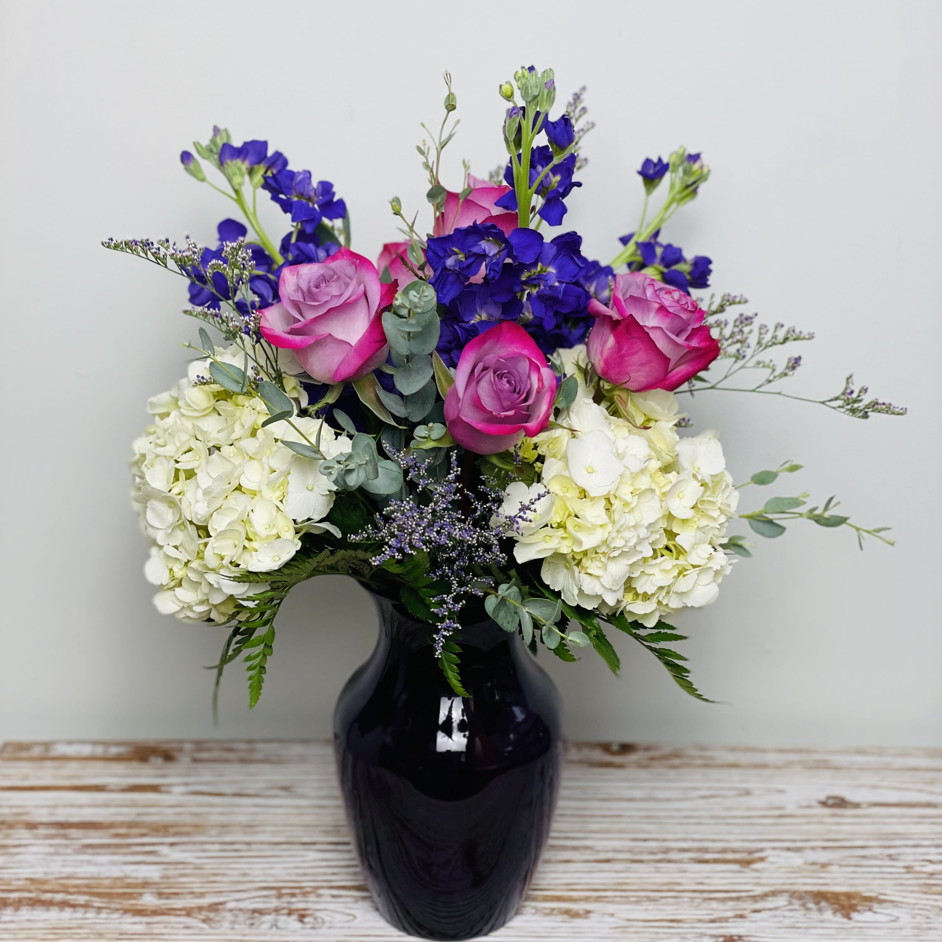 Pretty in Purple - Pretty in Purple is lovely assortment of fresh purple and lavender blooms of roses and sweet fragrant stock accented with hydrangea and limonium in a purple rose vase.   Approximately 16”-18” Tall  Container Country of Origin: USA Flower Country of Origin: Ecuador and/or Columbia