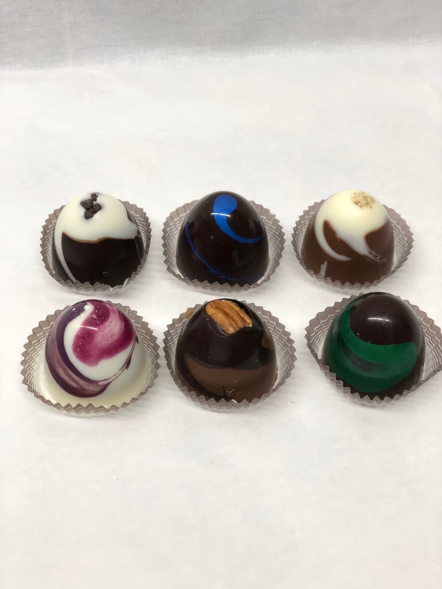 Set of six assorted round chocolate truffles in individual paper cups on a white surface