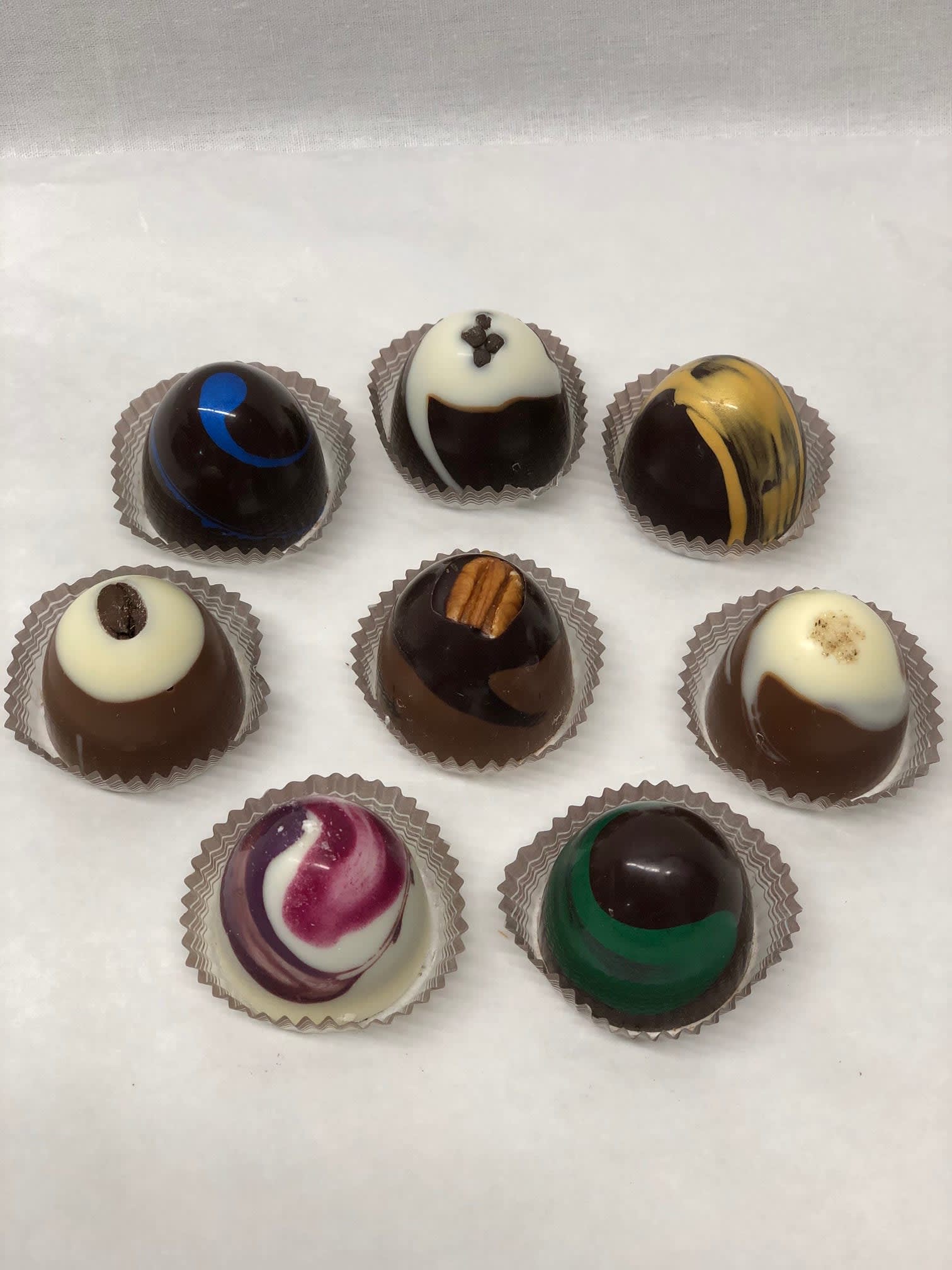 Assortment of eight decorated round chocolate truffles in paper cups on a white surface