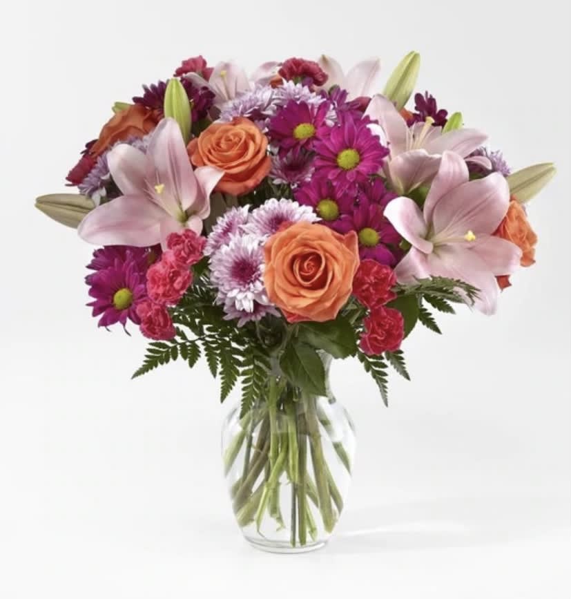 Mixed bouquet of lilies, roses, carnations, and mums in a clear glass vase