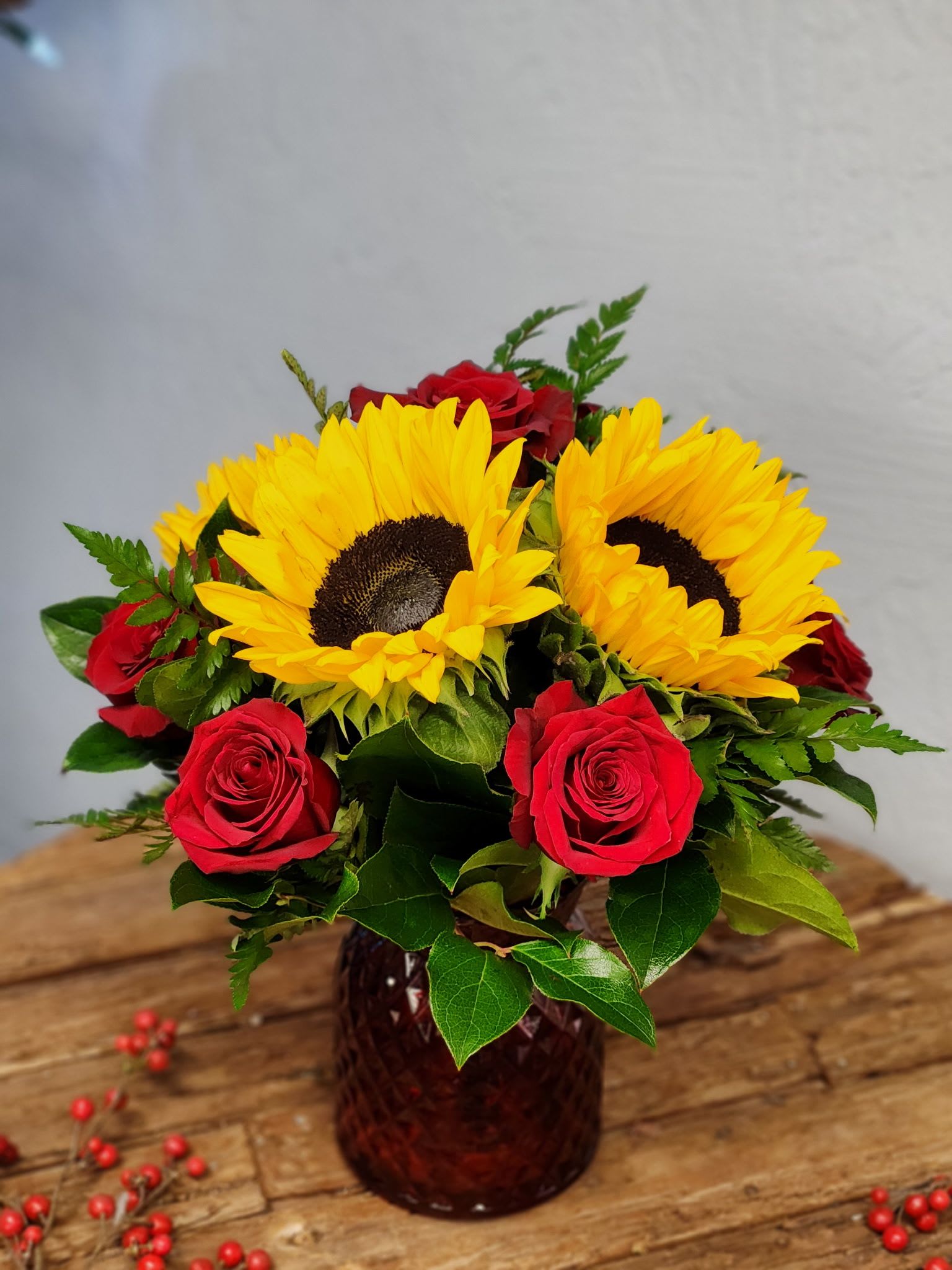 Arrangement of yellow sunflowers and red roses in a dark glass vase on a wooden table