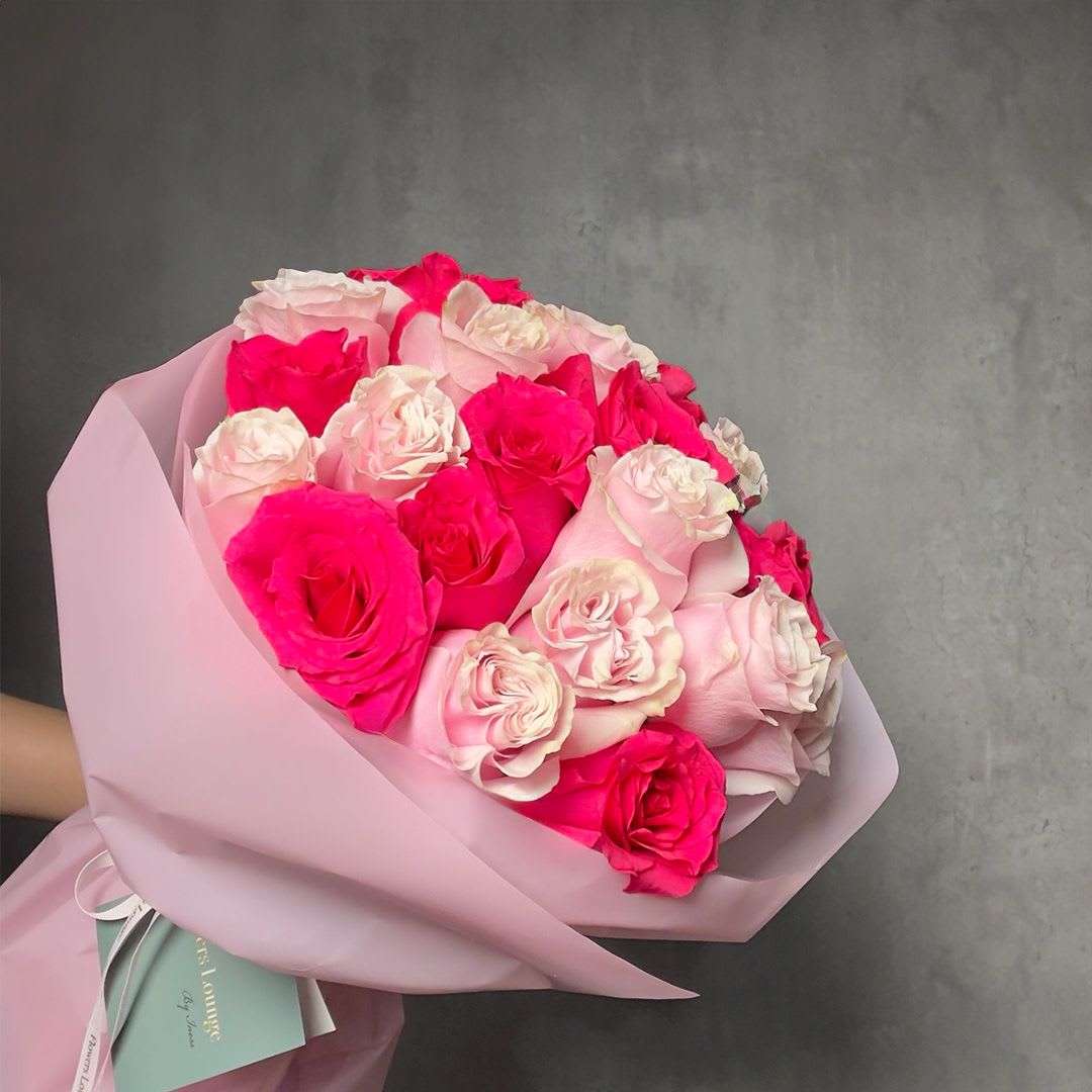 Hand-tied bouquet of bright and pale pink roses wrapped in soft pink paper