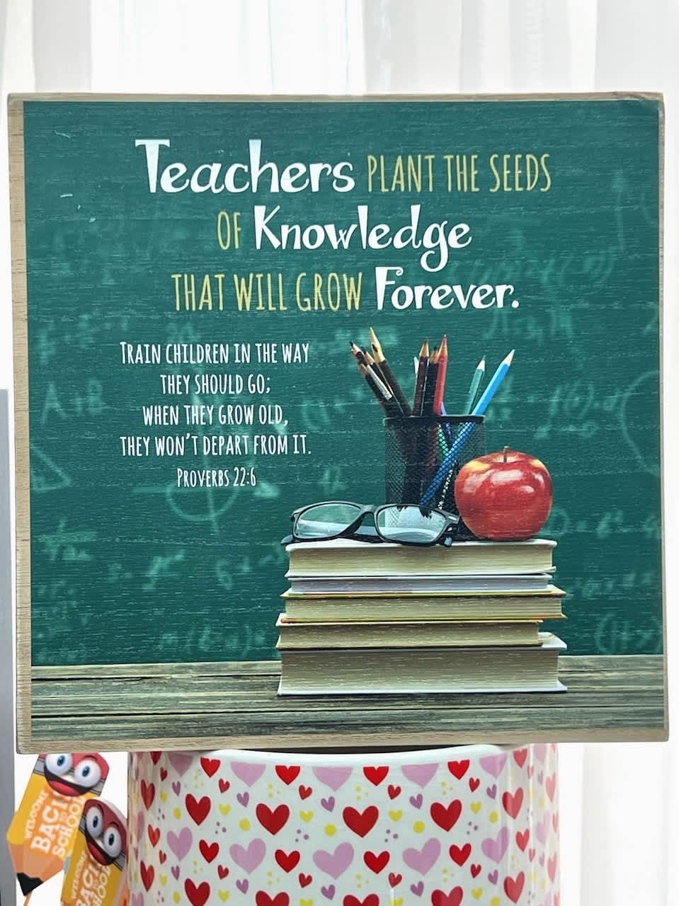 Teacher-themed sign with books, pencils, glasses, and an apple