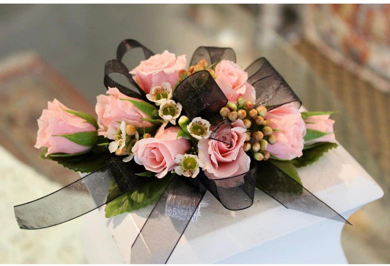 Corsage of pink roses with small white blossoms and black ribbon accents
