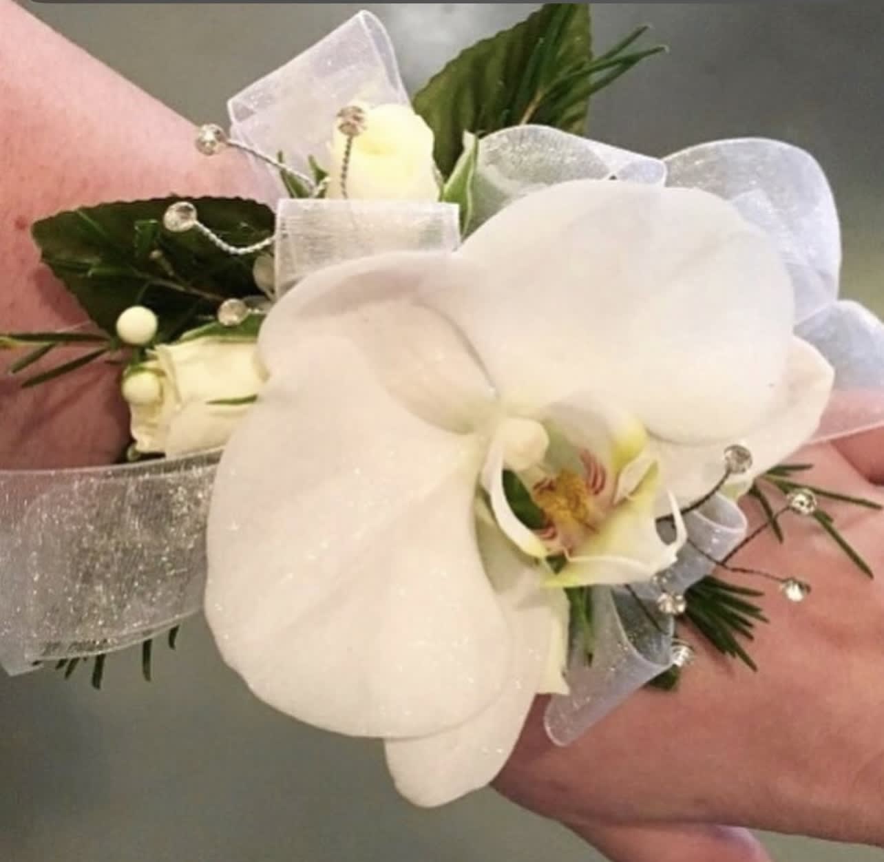 White orchid wrist corsage with sheer ribbon and small white buds on a wrist