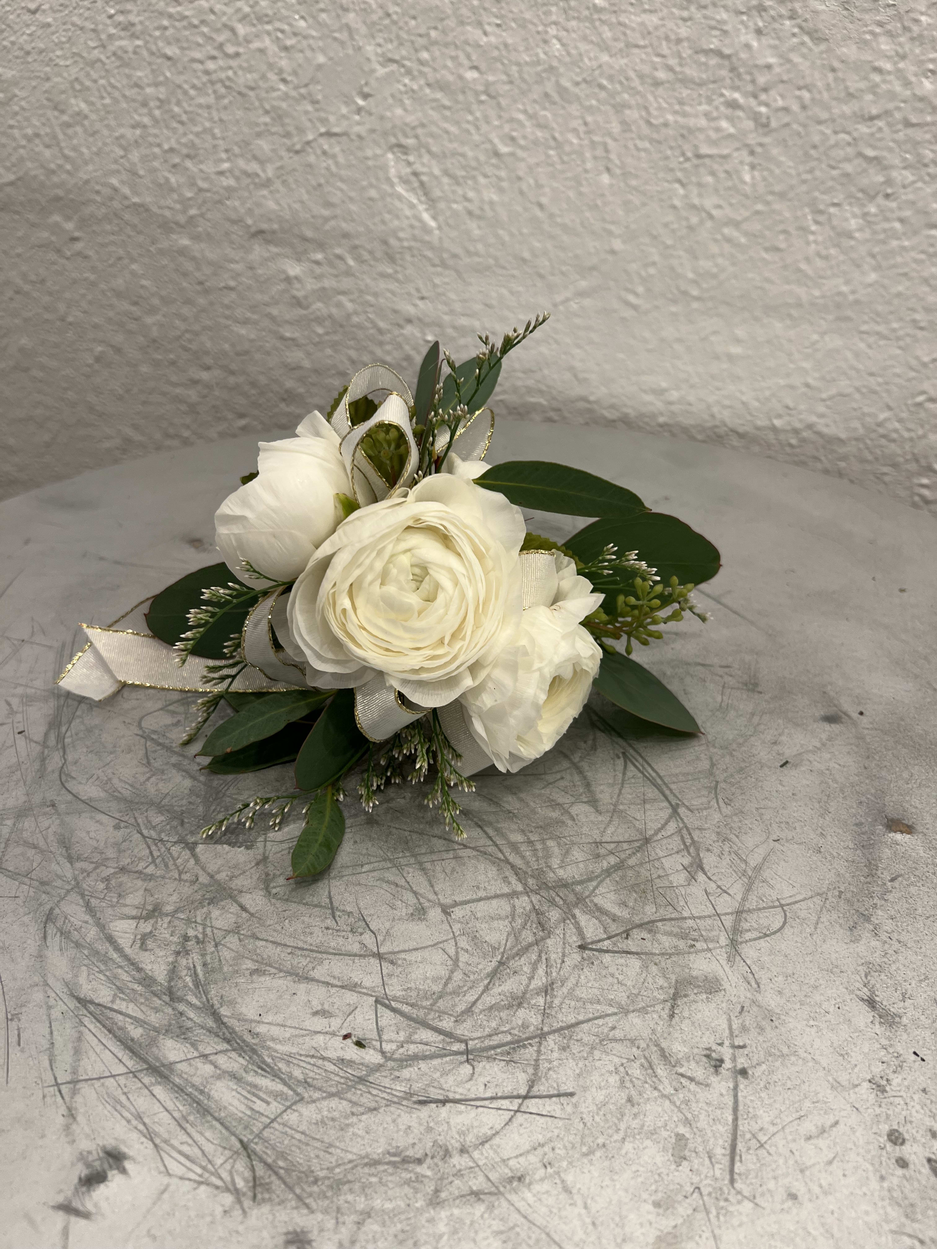 Small white ranunculus corsage with ribbon and foliage on a gray scratched surface