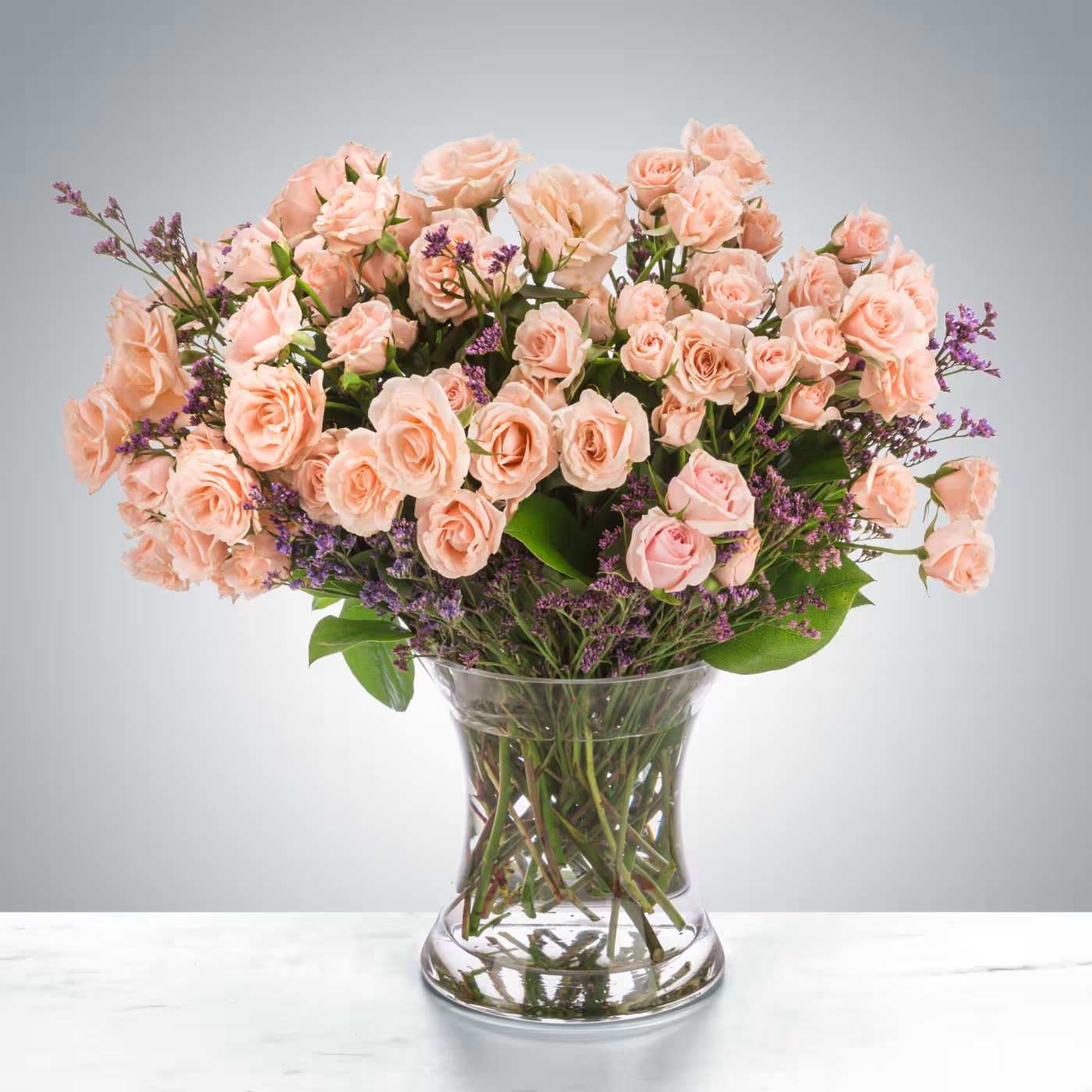 Large bouquet of peach spray roses with purple filler flowers in a clear glass vase