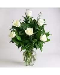 1/2 DOZEN WHITE ROSES - Pure white roses clustered with deep green foliage create a calm, elegant statement-perfect as a sympathy arrangement or understated anniversary bouquet. The half-dozen white roses sit slightly open to reveal soft petal layers, giving the recipient a sense of gentle comfort and timeless grace that reads as both sincere and refined.  Each stem is arranged upright in a simple clear glass vase, the gathered roses balanced by dense dark-green leaves for a rounded, classic silhouette. The vase comes filled with water for immediate display; this low-key, versatile design suits weddings, quiet celebrations, or a thoughtful way to say you're thinking of them-she'll feel steadied and seen when these arrive.