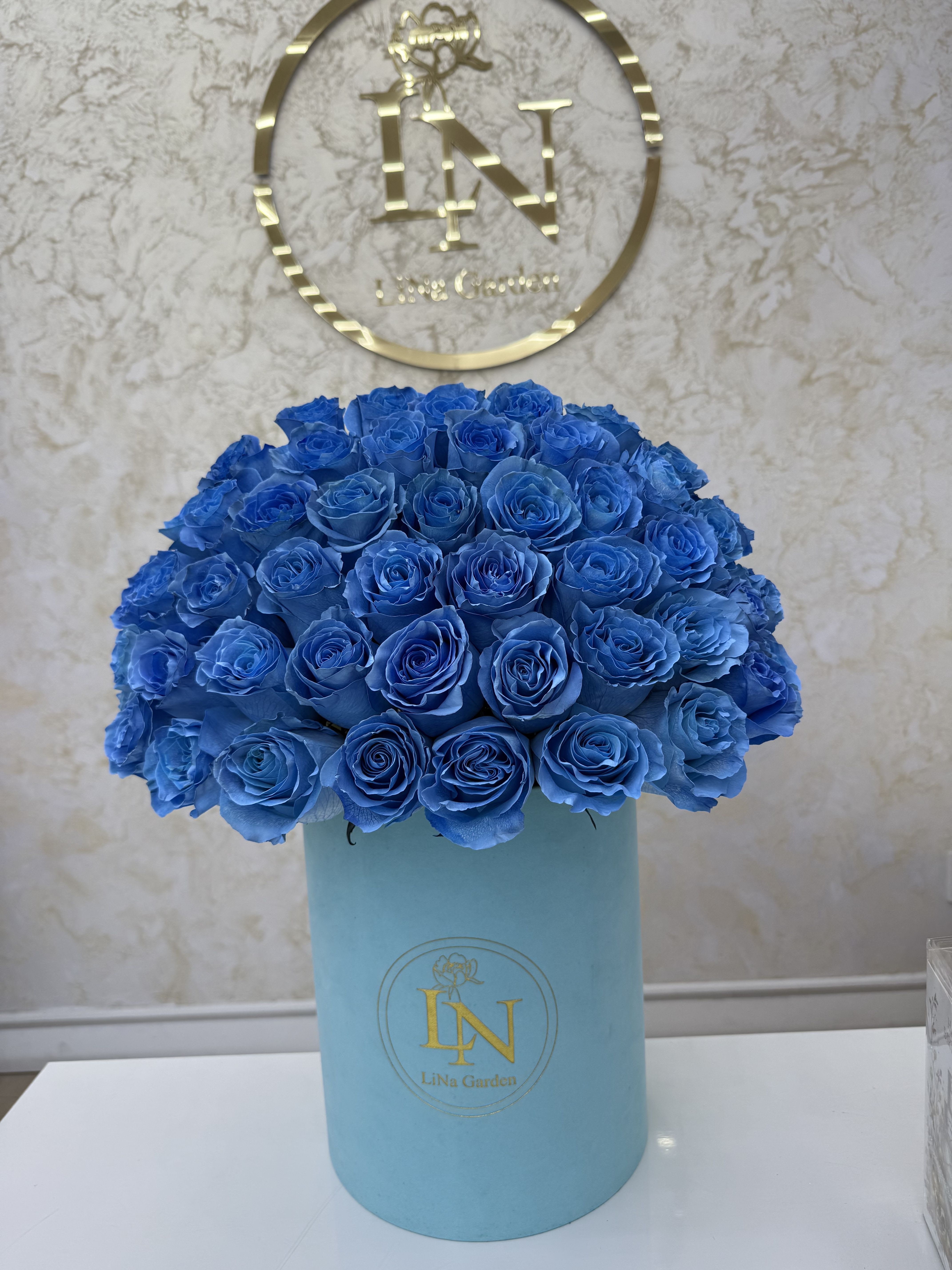 Dense arrangement of vivid blue roses in a light blue hatbox-style container.