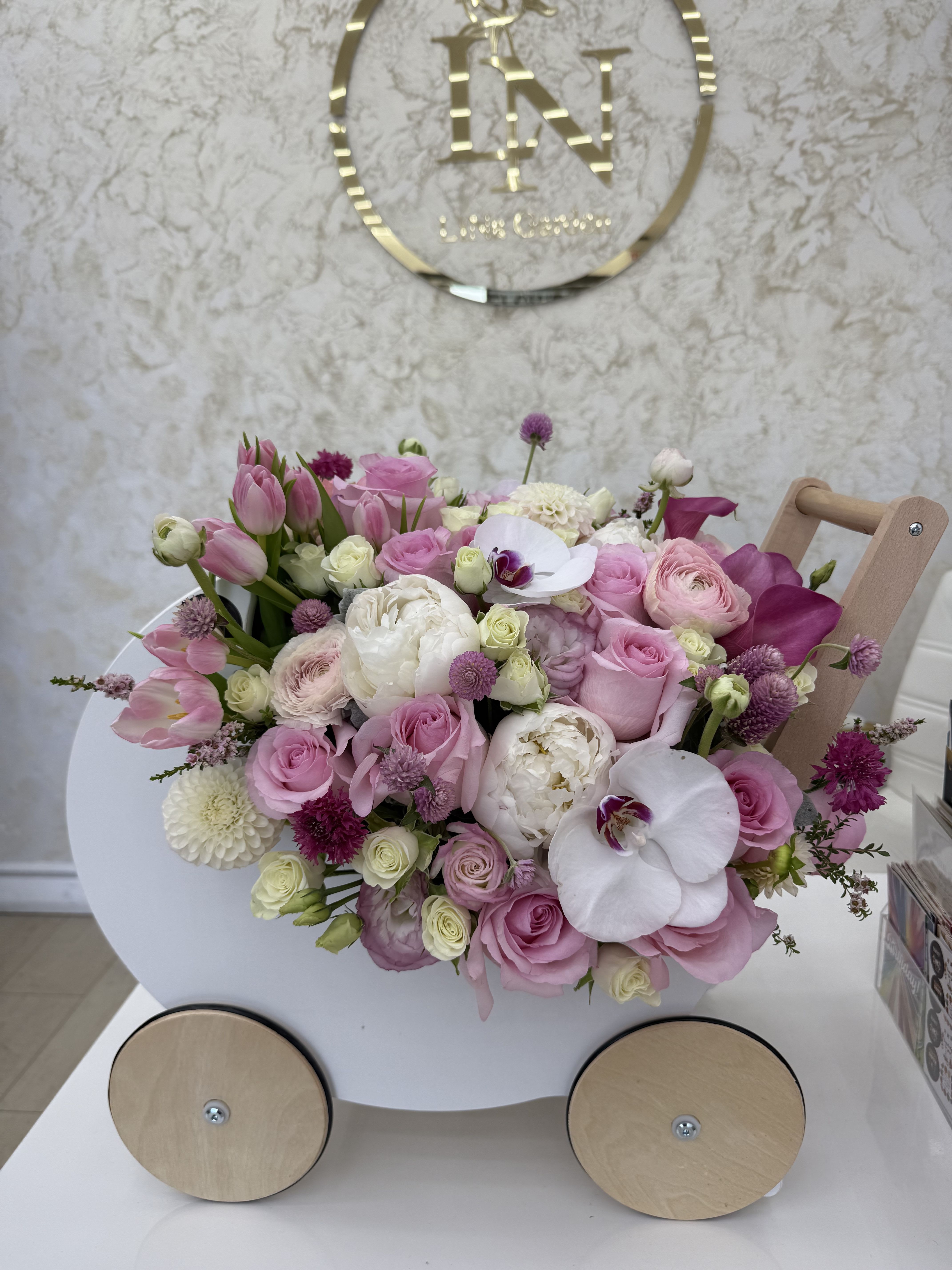 Pastel pink and white flower arrangement in a small white wooden cart with wheels.
