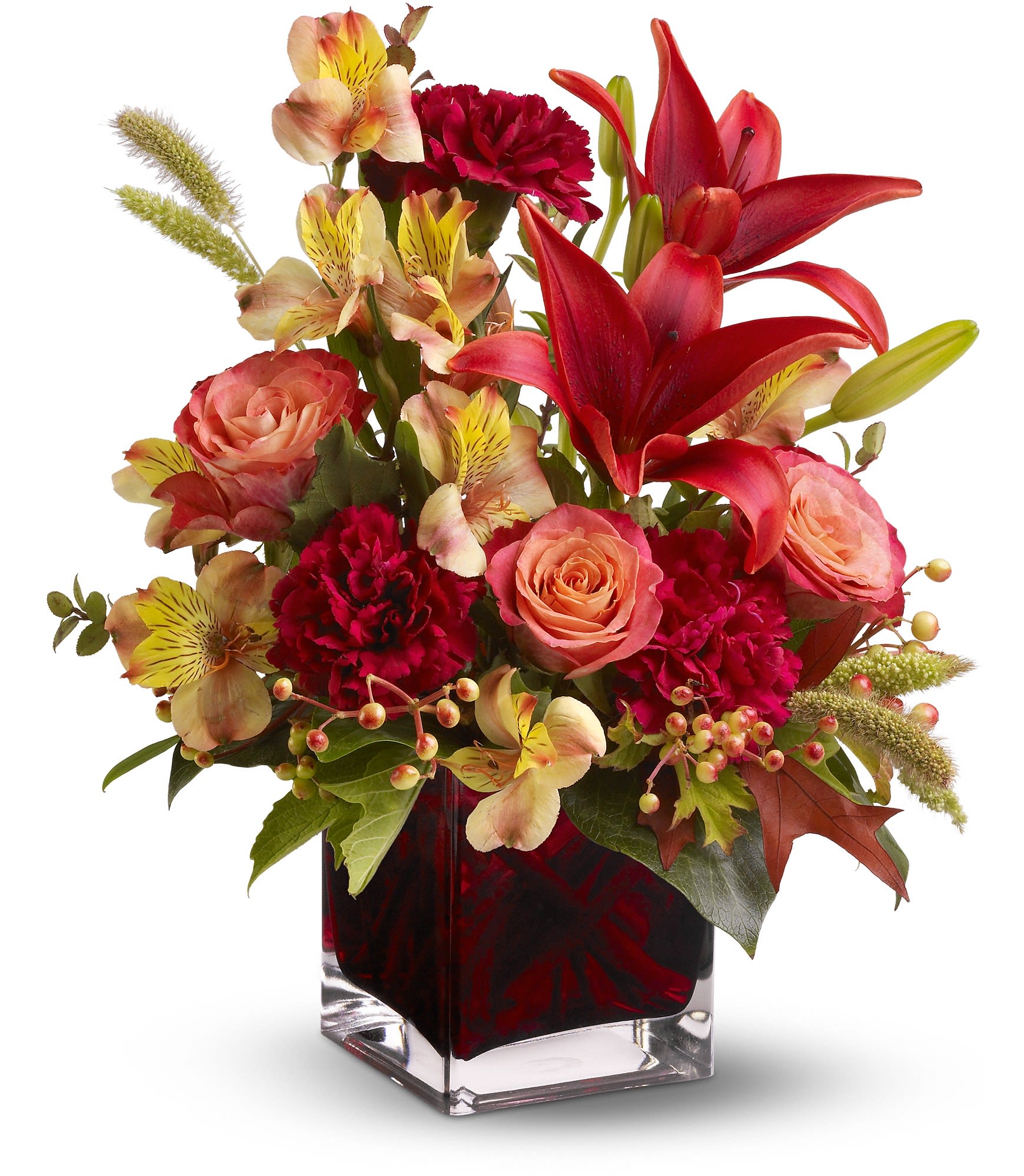 Compact arrangement of red lilies, roses, carnations, and alstroemeria in a square glass vase
