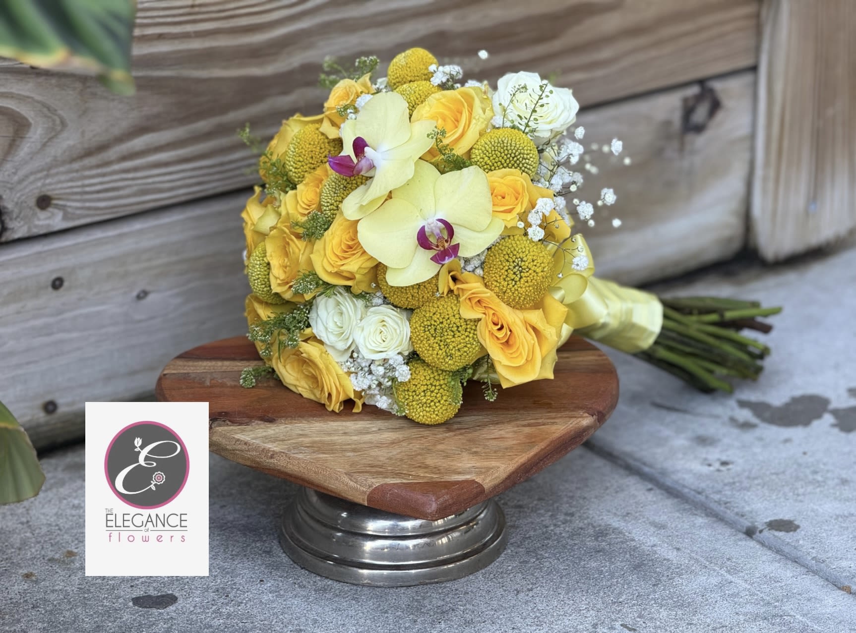 Hand-tied bouquet of yellow roses and pale orchids resting on a wooden pedestal.