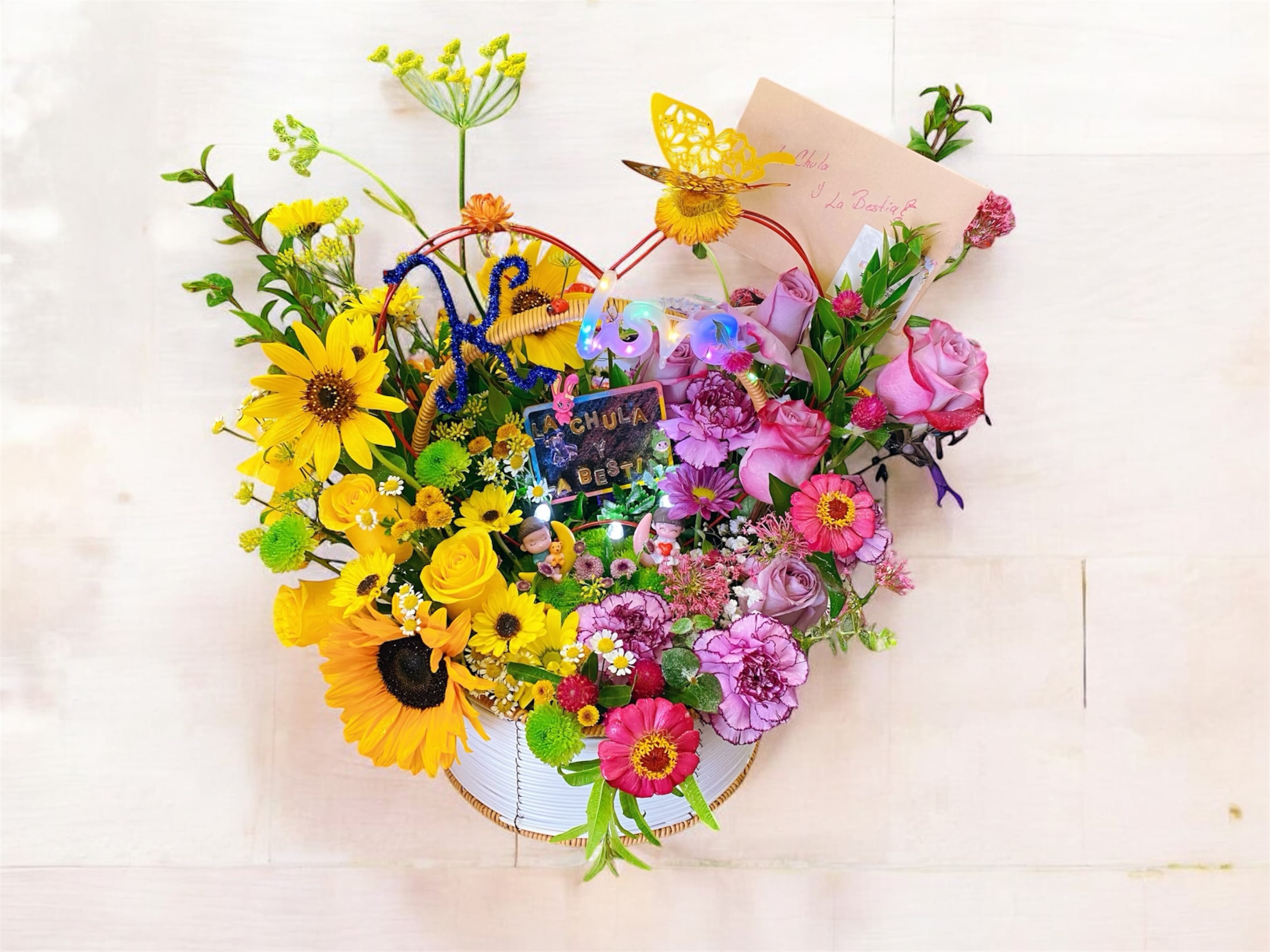 Colorful basket arrangement with yellow sunflowers and roses on one side and pink roses and carnations on the other.