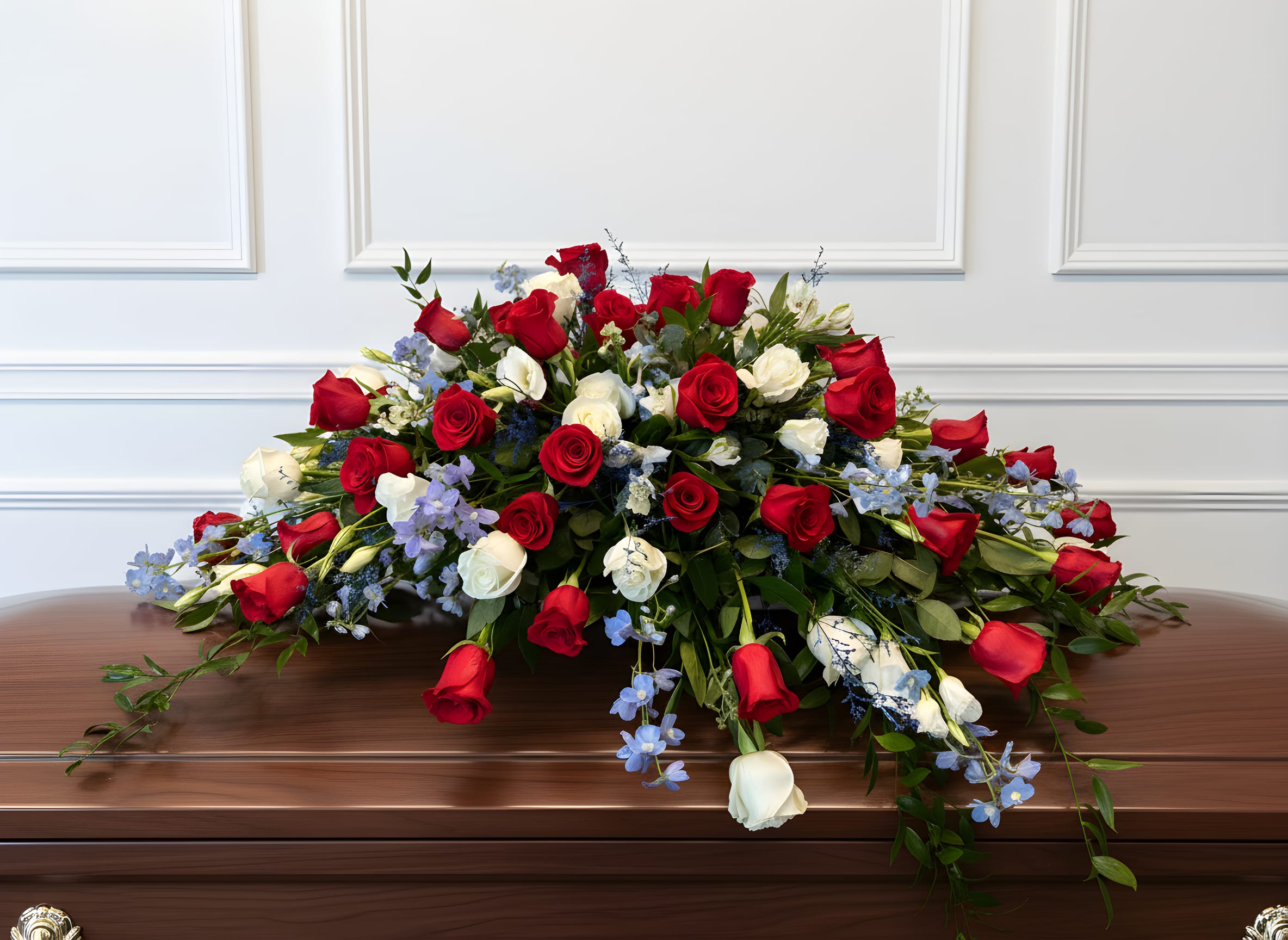 Patriotic Honor Casket Spray - Honor a life of strength, love, and legacy with our Patriotic Honor Casket Spray. This striking floral tribute features a bold and meaningful combination of red roses, white blooms, and soft blue accents, thoughtfully arranged with lush greenery to create a full and flowing design.  Symbolizing love, respect, and remembrance, the red, white, and blue palette offers a powerful tribute perfect for honoring veterans, first responders, or anyone who lived with pride and strength.  Designed to rest gracefully atop the casket, this arrangement creates a dignified and heartfelt presence during funeral services, memorials, or celebration of life ceremonies.  Each piece is handcrafted with care and compassion, ensuring a meaningful and beautiful tribute that reflects honor, love, and lasting memory.  Serving Rancho Cucamonga and the Inland Empire, we are honored to help you express your sympathy with dignity, respect, and heartfelt intention.