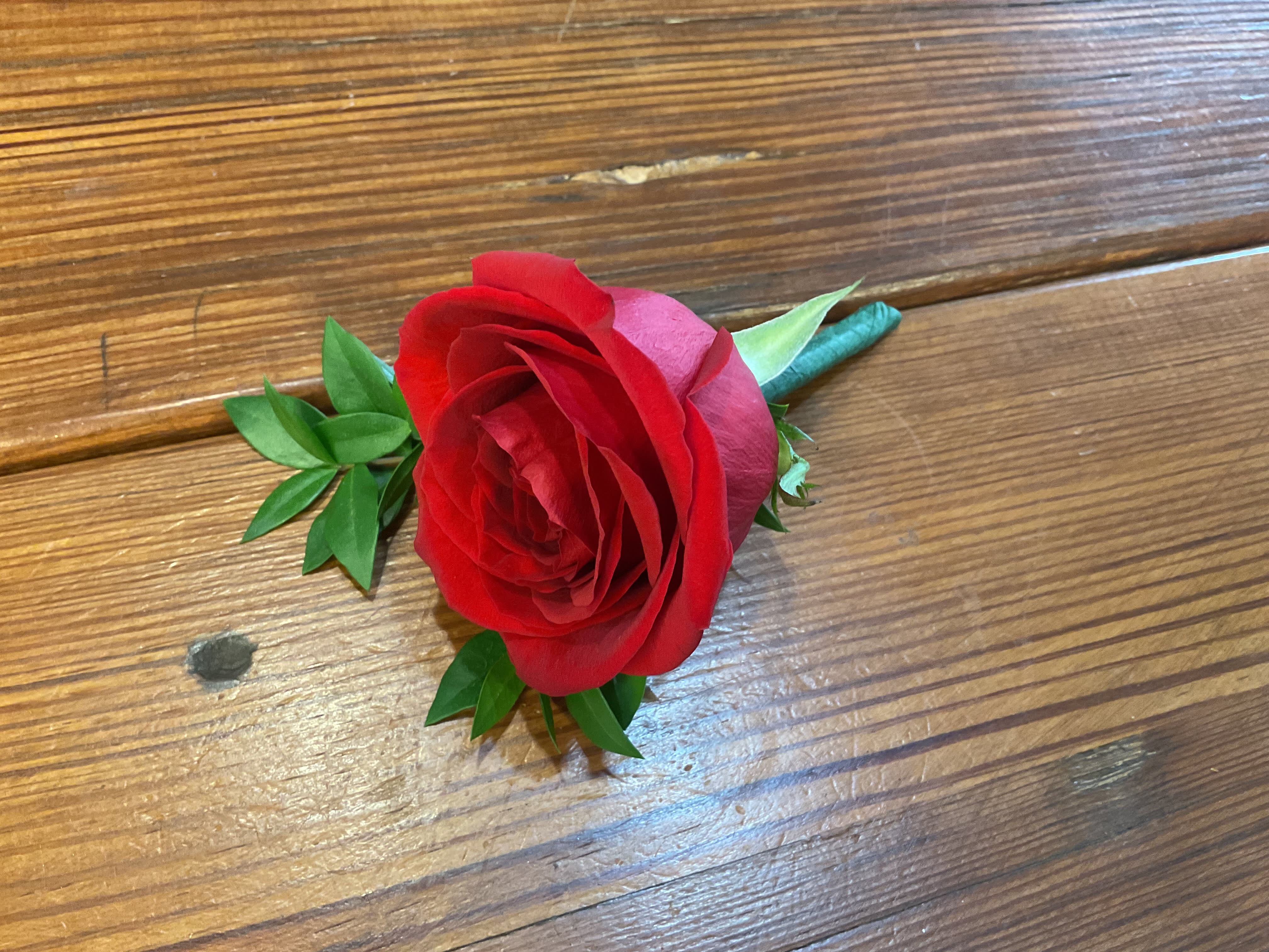 Single red rose boutonniere with wrapped stem on a wooden surface