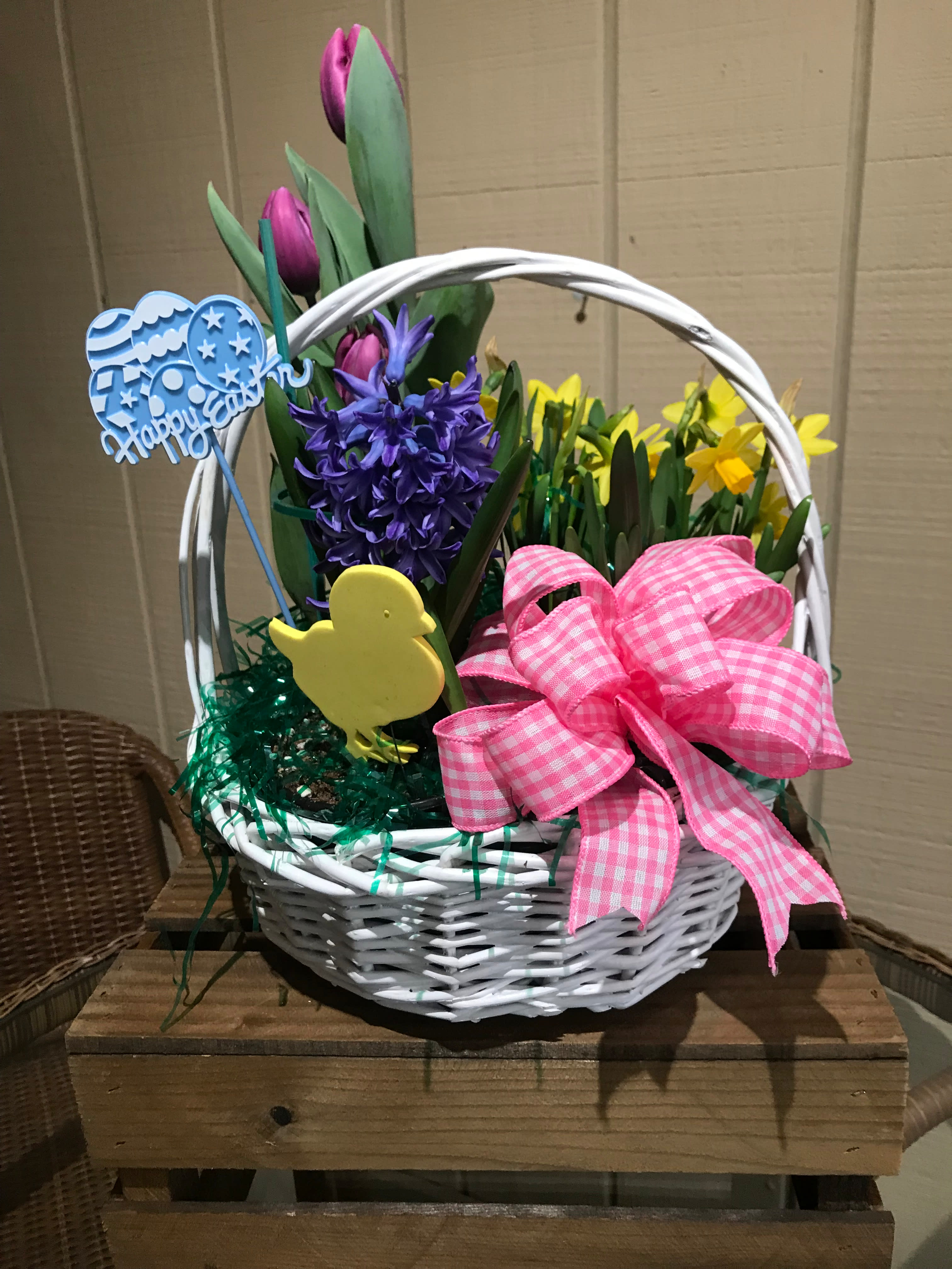 Easter basket of purple tulips, hyacinth, and yellow daffodils with a pink bow and festive decorations.