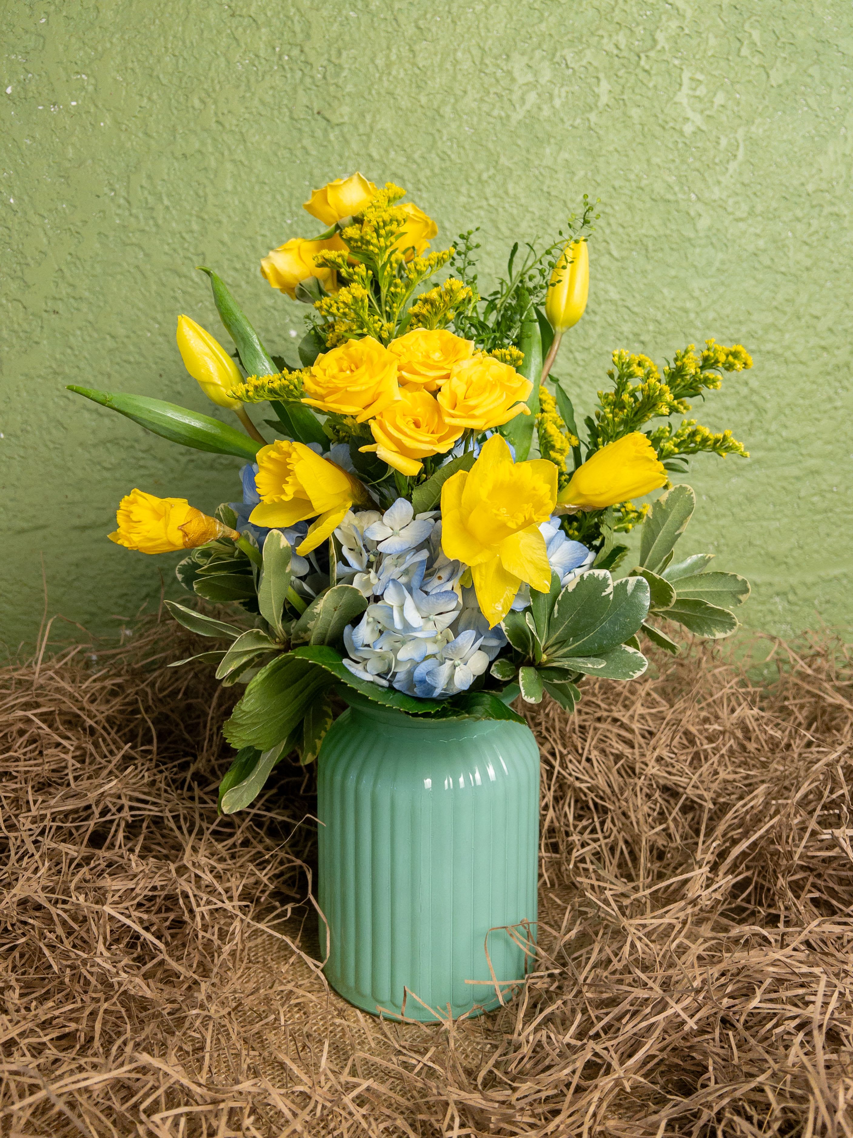 Blue Bunny Arrangement - The Blue Bunny is a petite arrangement in cheerful yellow and blue hues, featuring tulips, daffodils, roses, solidago, and pittosporum. Its playful colors and Easter-inspired charm make it a perfect centerpiece for your home or a delightful gift. Trust your local Baltimore Florist for same-day Flower Delivery in Baltimore, bringing a touch of springtime whimsy right to your door.