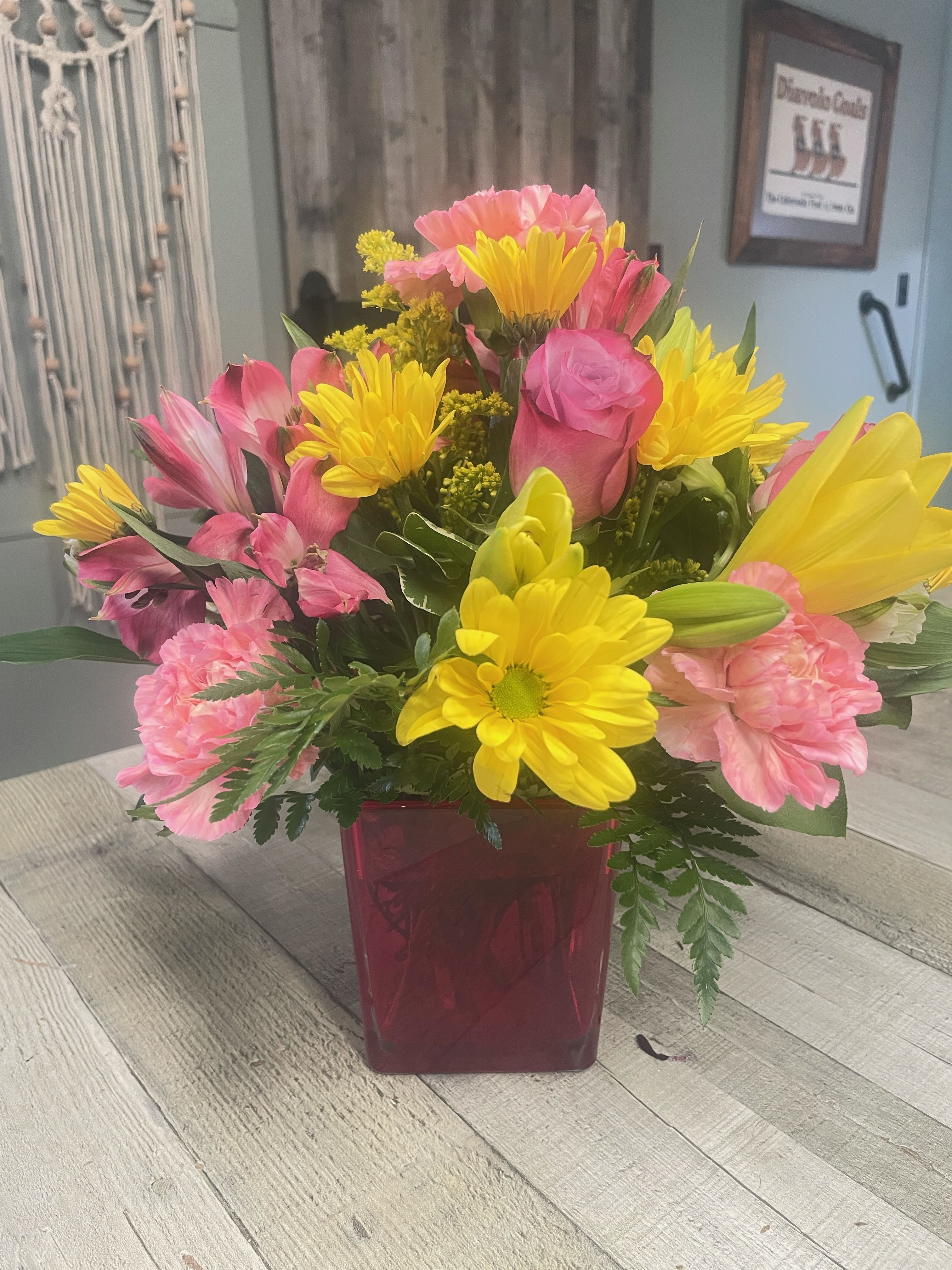 Bright bouquet of yellow daisies and pink roses in a red glass cube vase