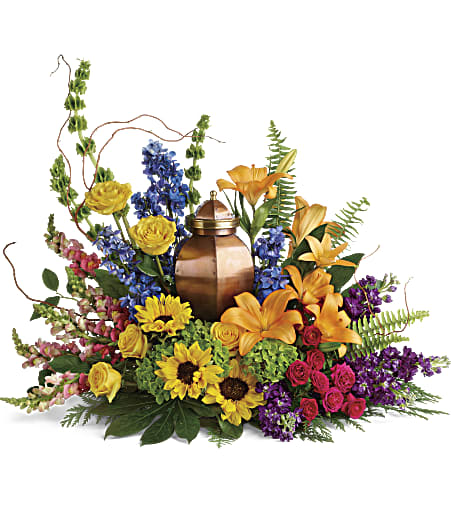 Low ring of colorful lilies, roses, sunflowers, and other blooms surrounding a bronze urn.