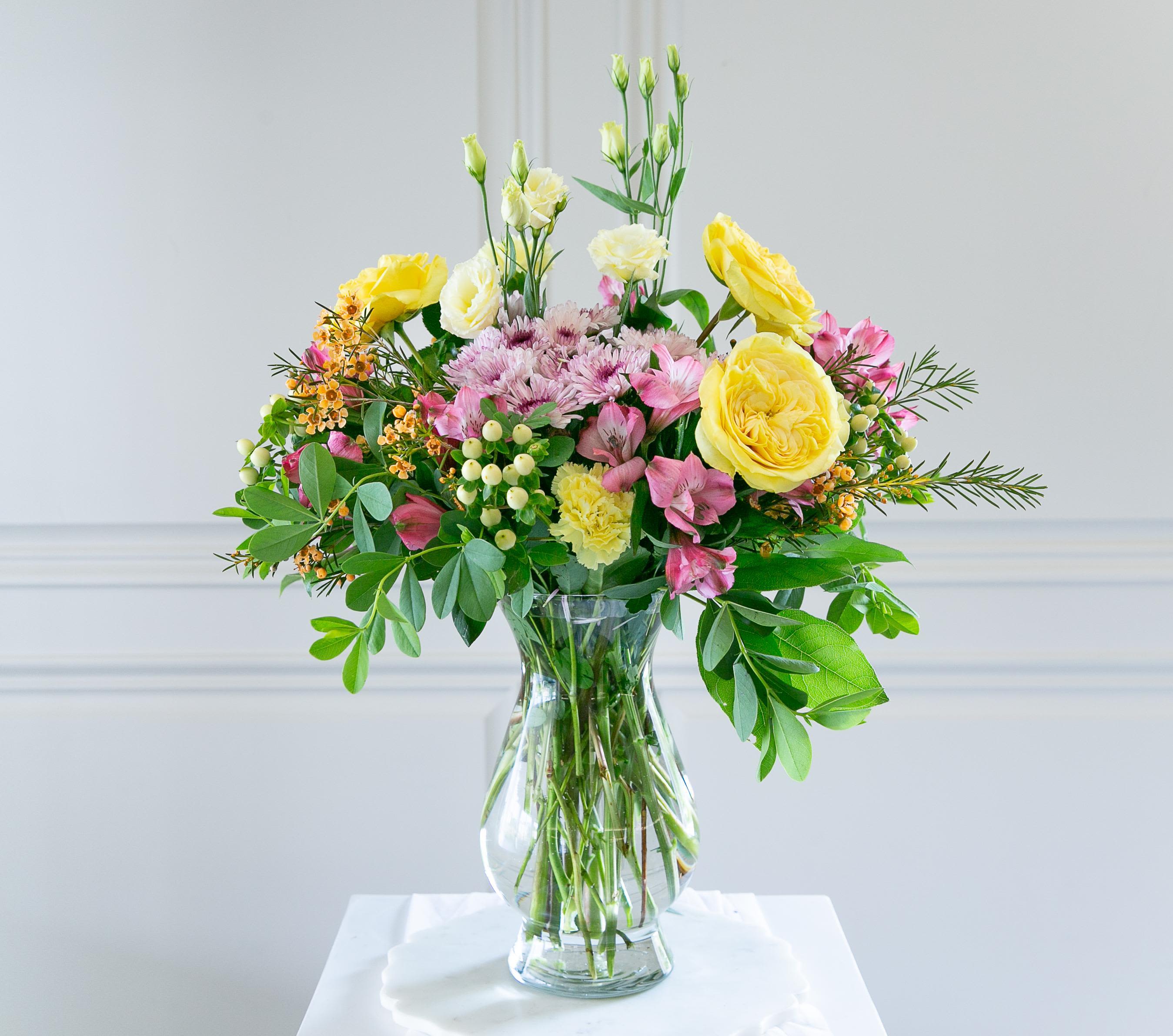 Mixed bouquet of yellow and pink flowers in a clear glass vase on a white surface