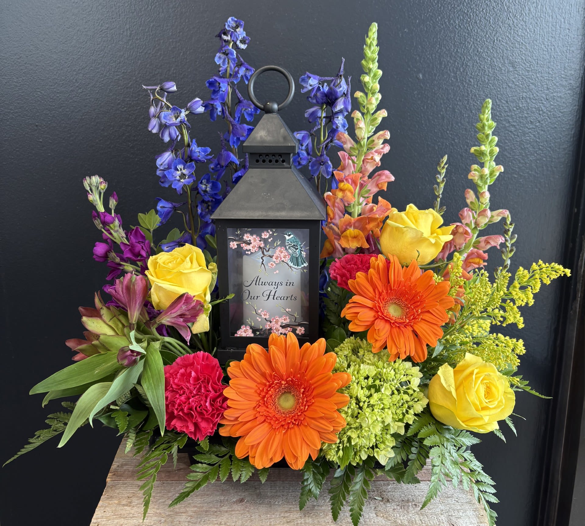 Colorful sympathy lantern arrangement with roses and gerbera daisies