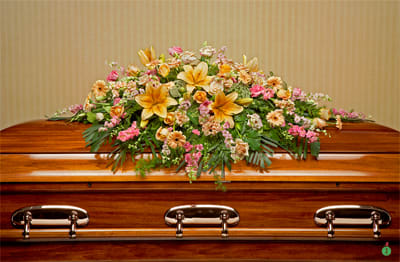 Casket spray of yellow lilies, peach and pink flowers with cascading greenery on a wooden casket