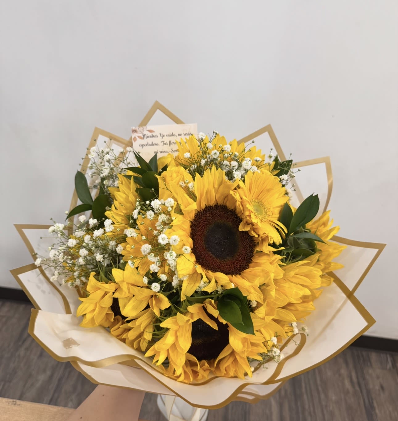 Hand-tied bouquet of bright yellow sunflowers and tiny white blooms wrapped in cream and gold paper