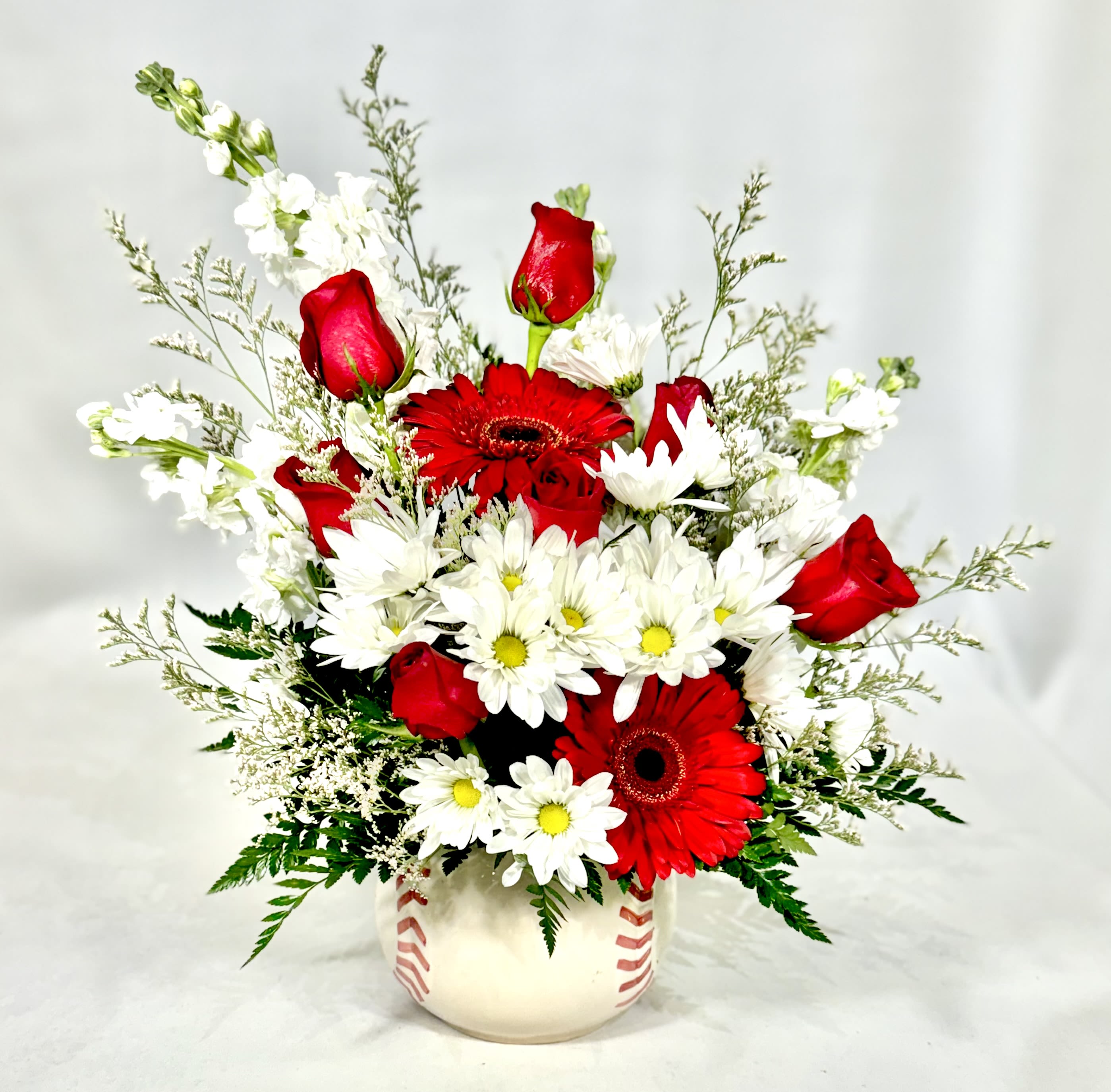 Red roses, red gerbera daisies, and white daisies arranged in a baseball-themed ceramic vase
