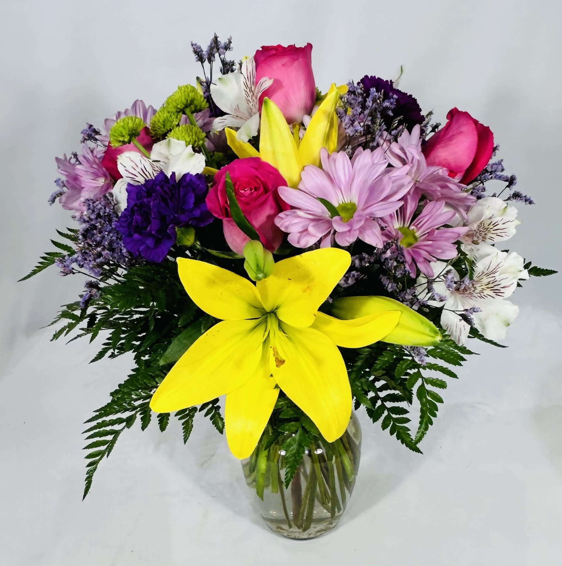 Mixed bouquet of yellow lilies, pink roses, and assorted blooms in a clear glass vase