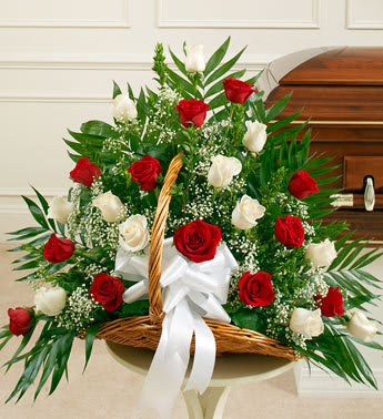 Basket arrangement of red and white roses with a white bow in front of a casket.
