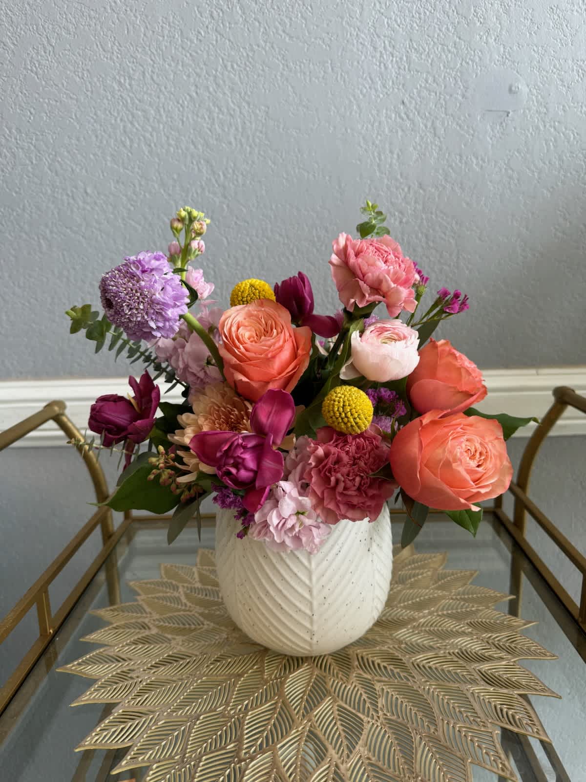 Colorful arrangement of pink, orange, and purple flowers in a white textured vase on a glass cart